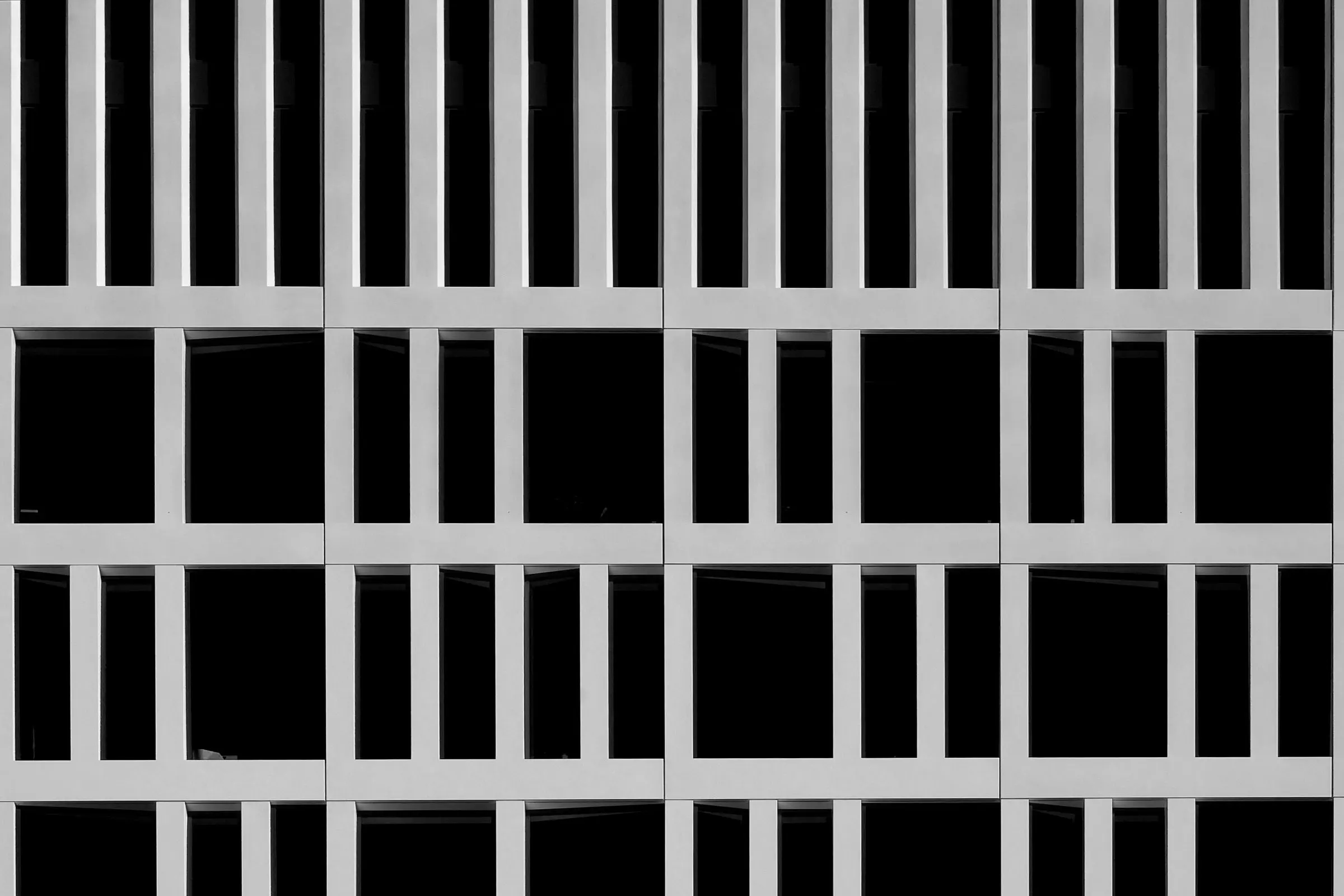 Facciata in bianco e nero di un edificio scolastico: griglia regolare di pilastri e marcapiani in cemento