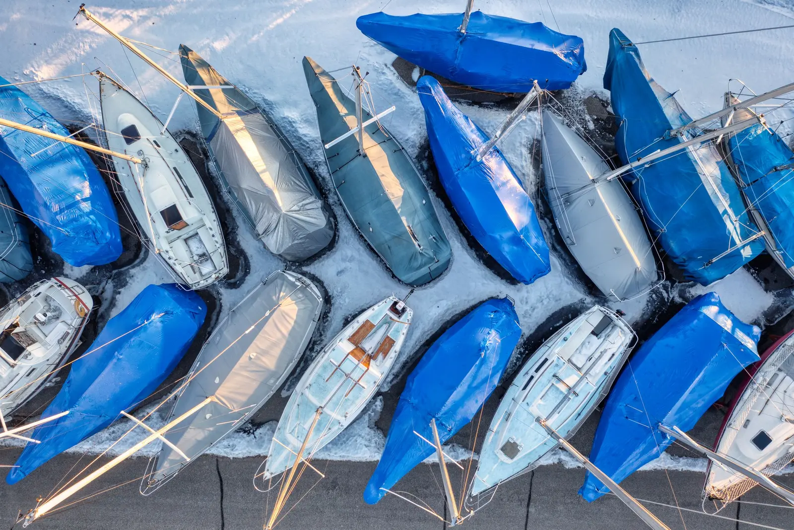 Barche a vela a terra viste dall'alto, in file a spina di pesce, molte coperte da teli blu