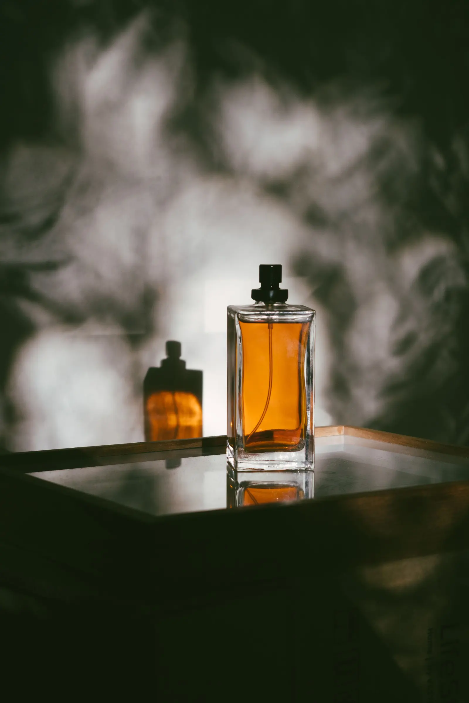 Un flacone di profumo ambrato appoggiato su uno specchio, tra le ombre delle foglie