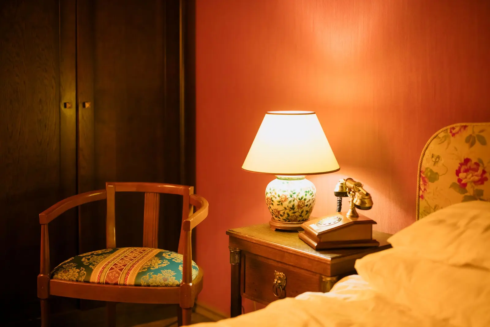 Comodino in legno con lampada accesa e telefono d'epoca contro una parete arancio