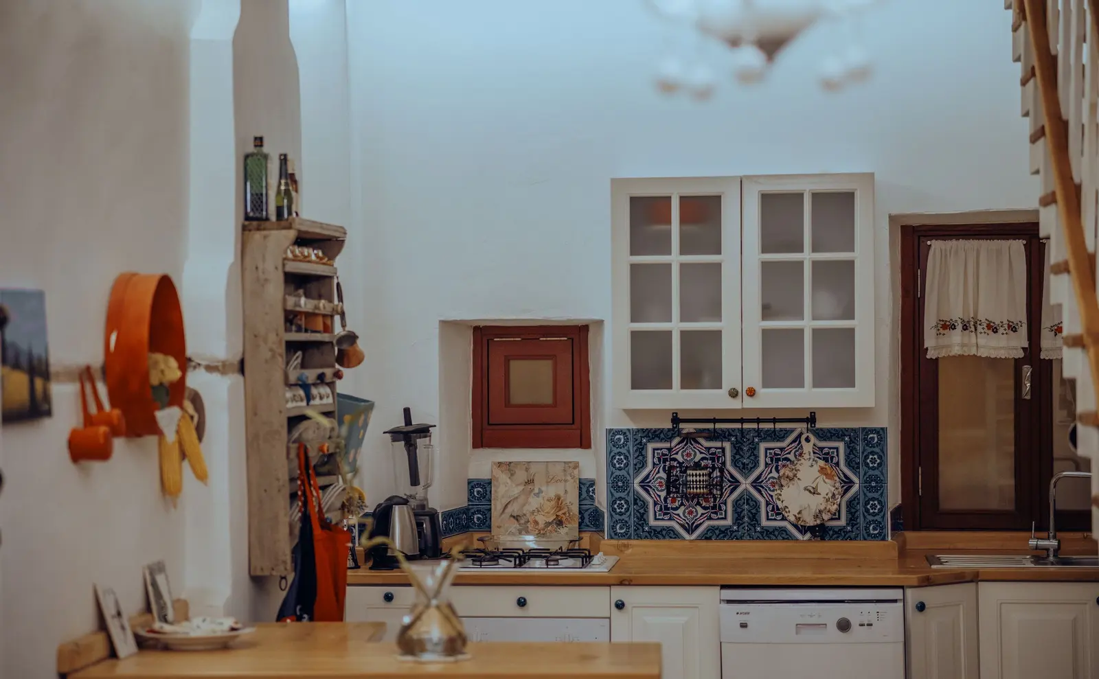 Cucina bianca con piastrelle blu dipinte, piano in legno e mensole con barattoli