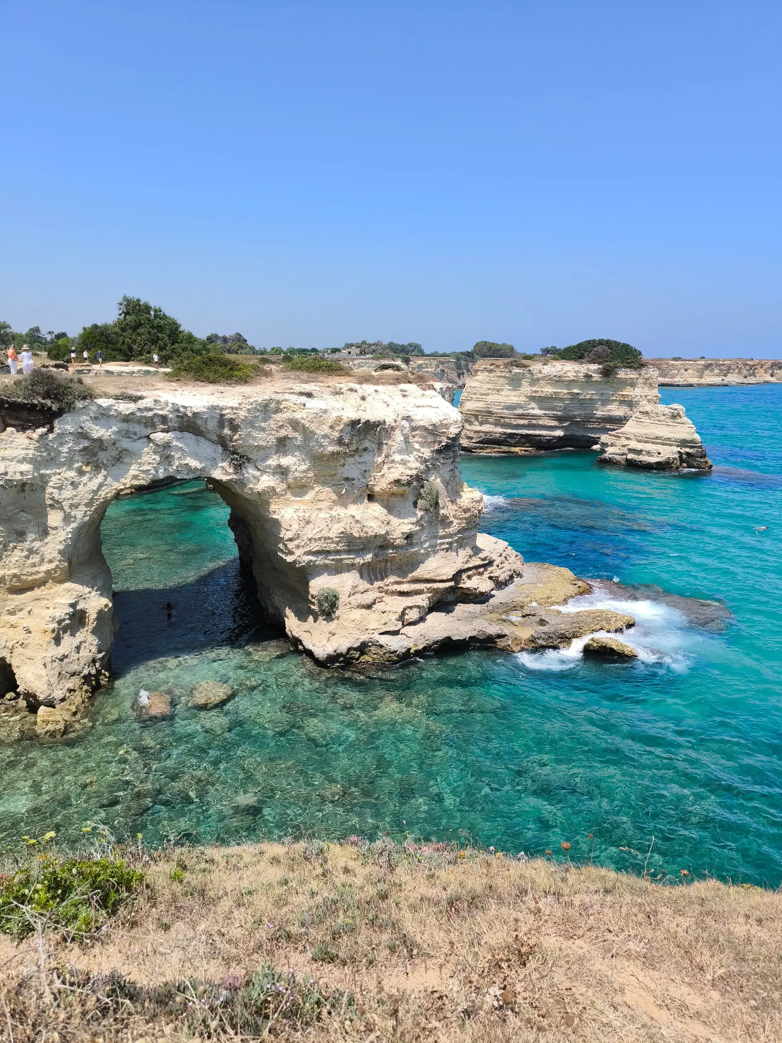 Scogliera chiara con un arco naturale nella roccia e l'acqua turchese sotto