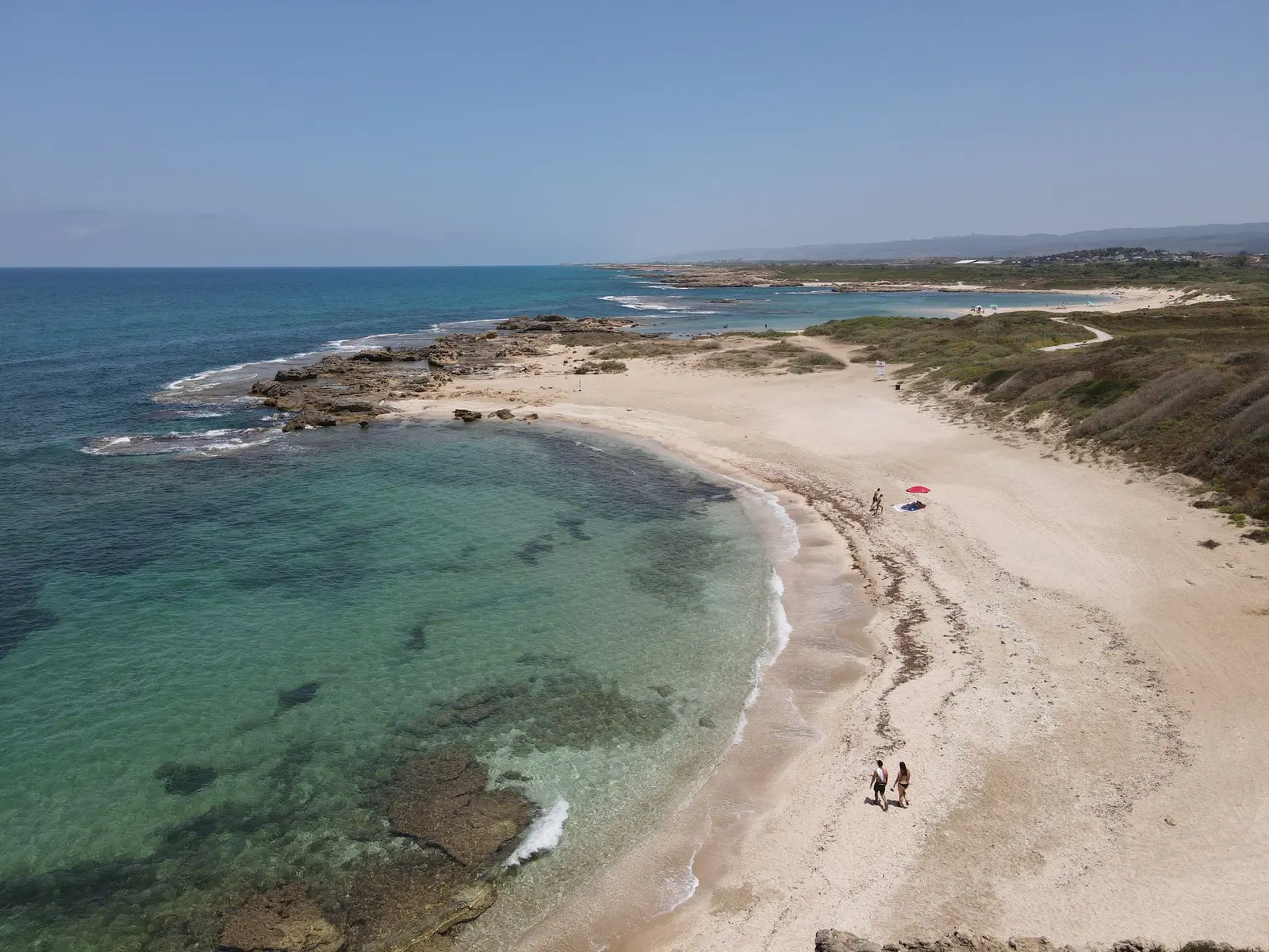 Spiaggia di sabbia a mezzaluna vista dall'alto, acqua bassa e quasi nessuno