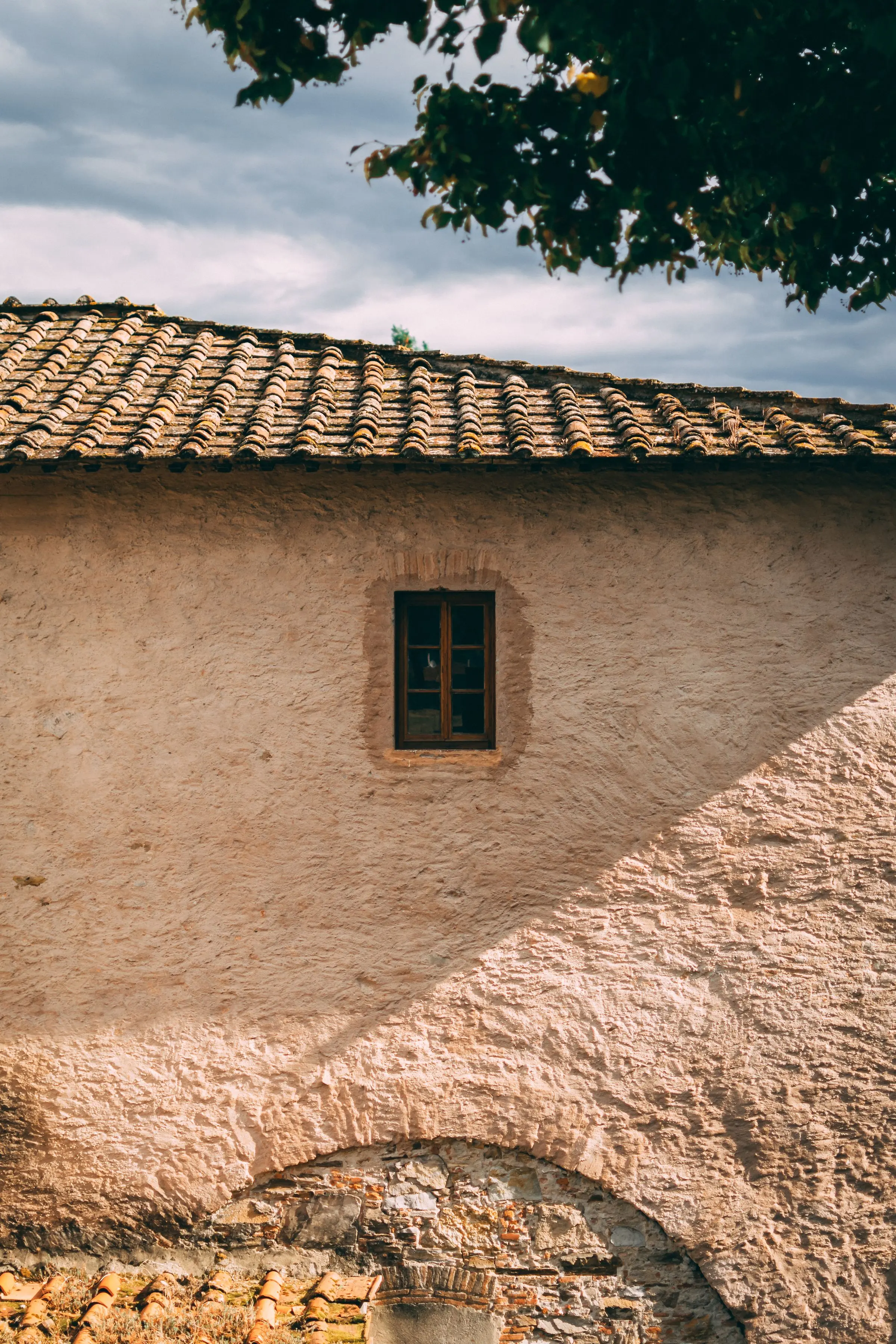 Angolo di una casa con intonaco a calce consumato, una finestra piccola e la gronda in coppi