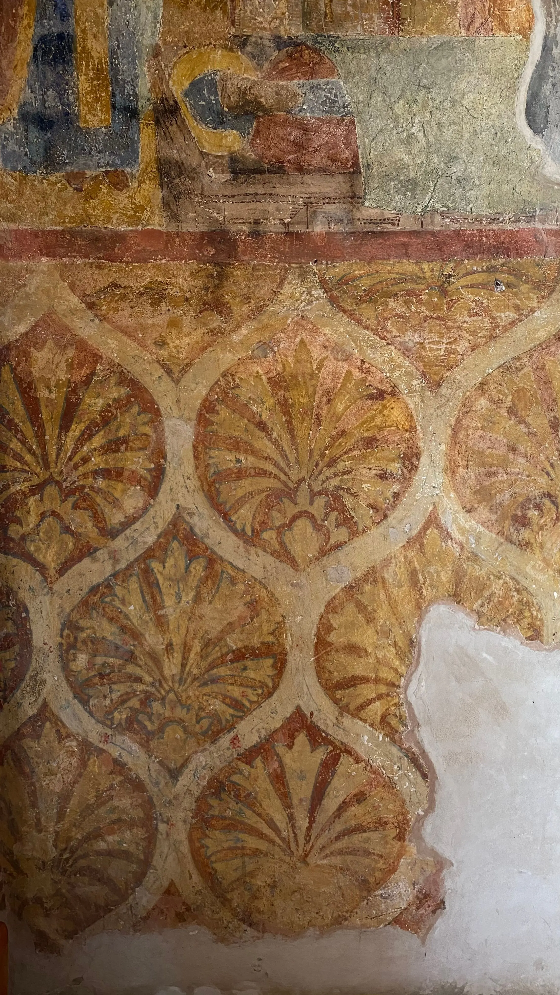 Decorazione dipinta a motivi vegetali color ocra, interrotta da una lacuna d'intonaco