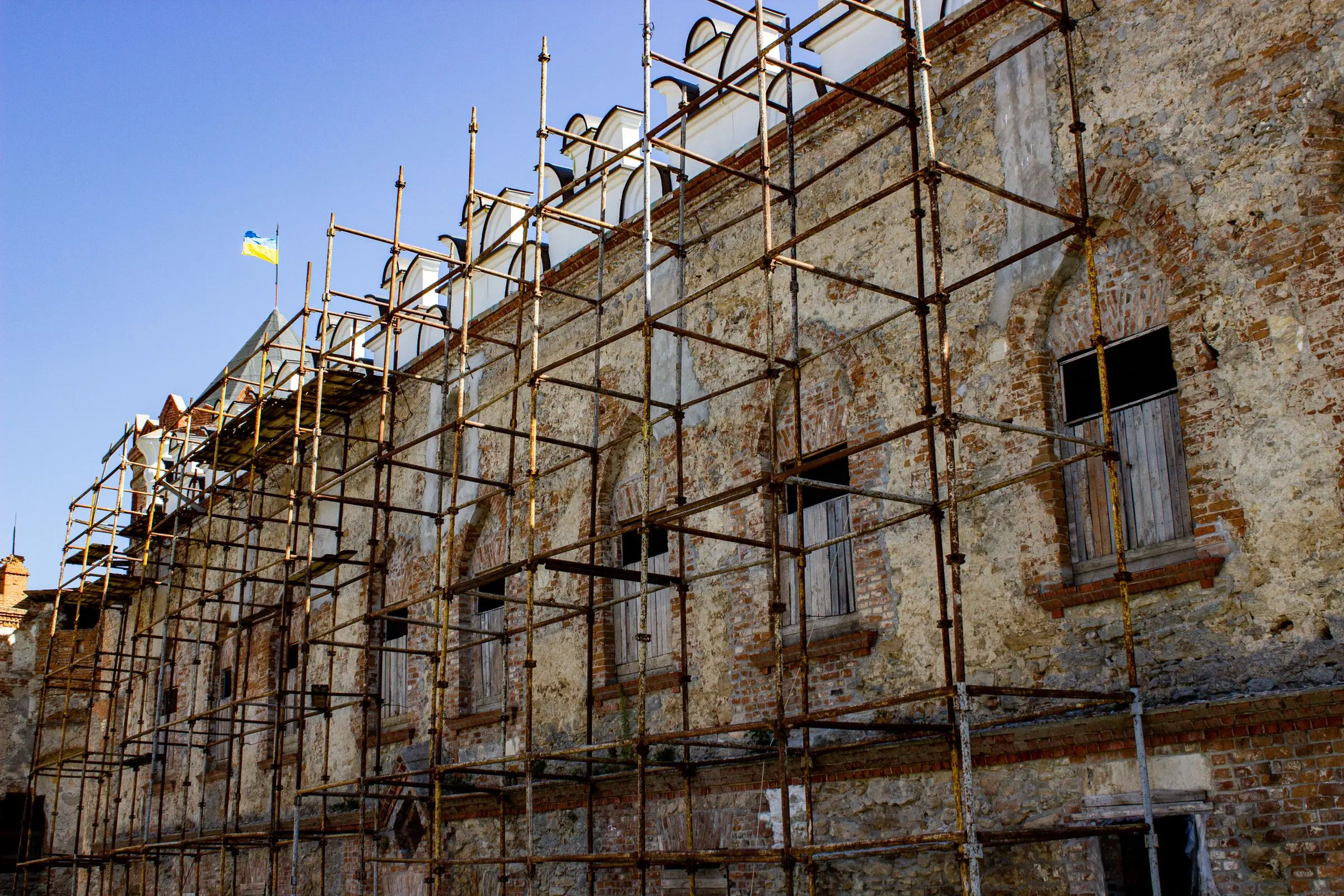 Ponteggio montato lungo la facciata di un edificio storico in mattoni e intonaco, con finestre ad arco