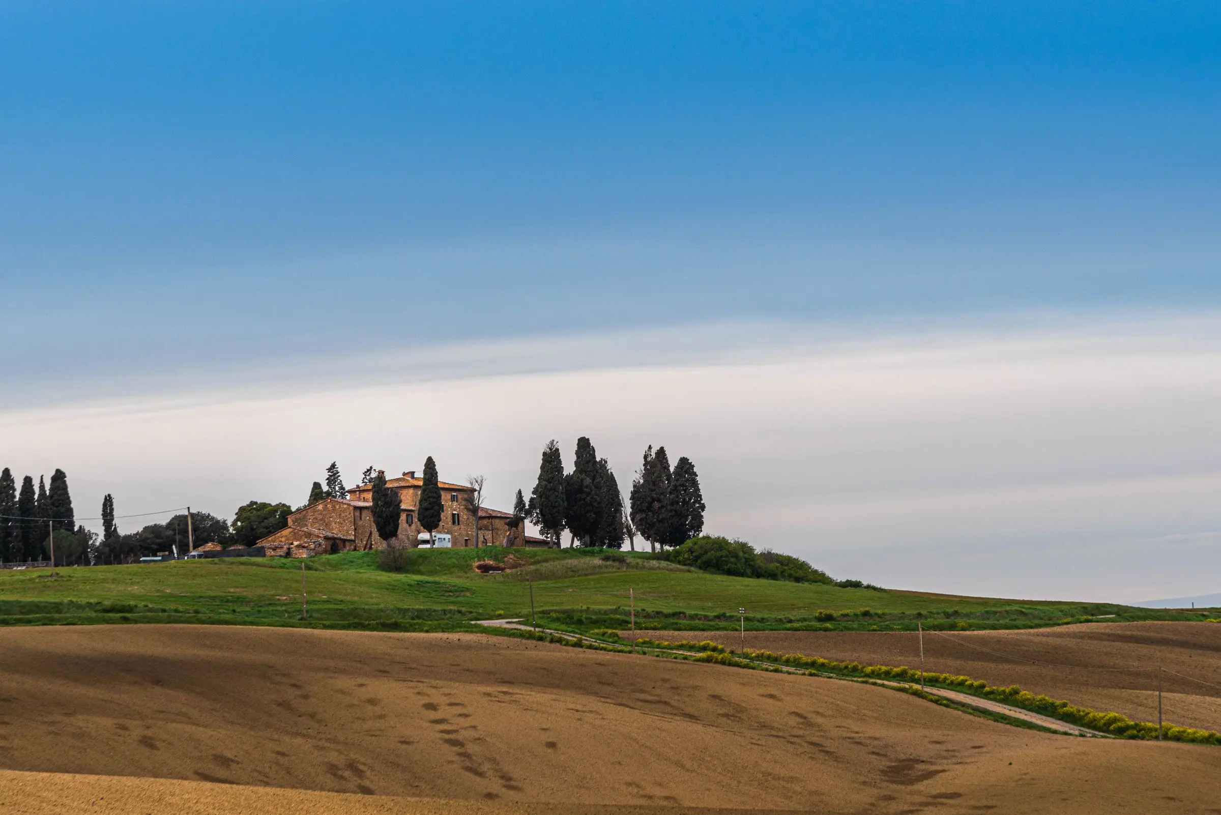 Colline coltivate della Toscana meridionale con un casale e una fila di cipressi in lontananza