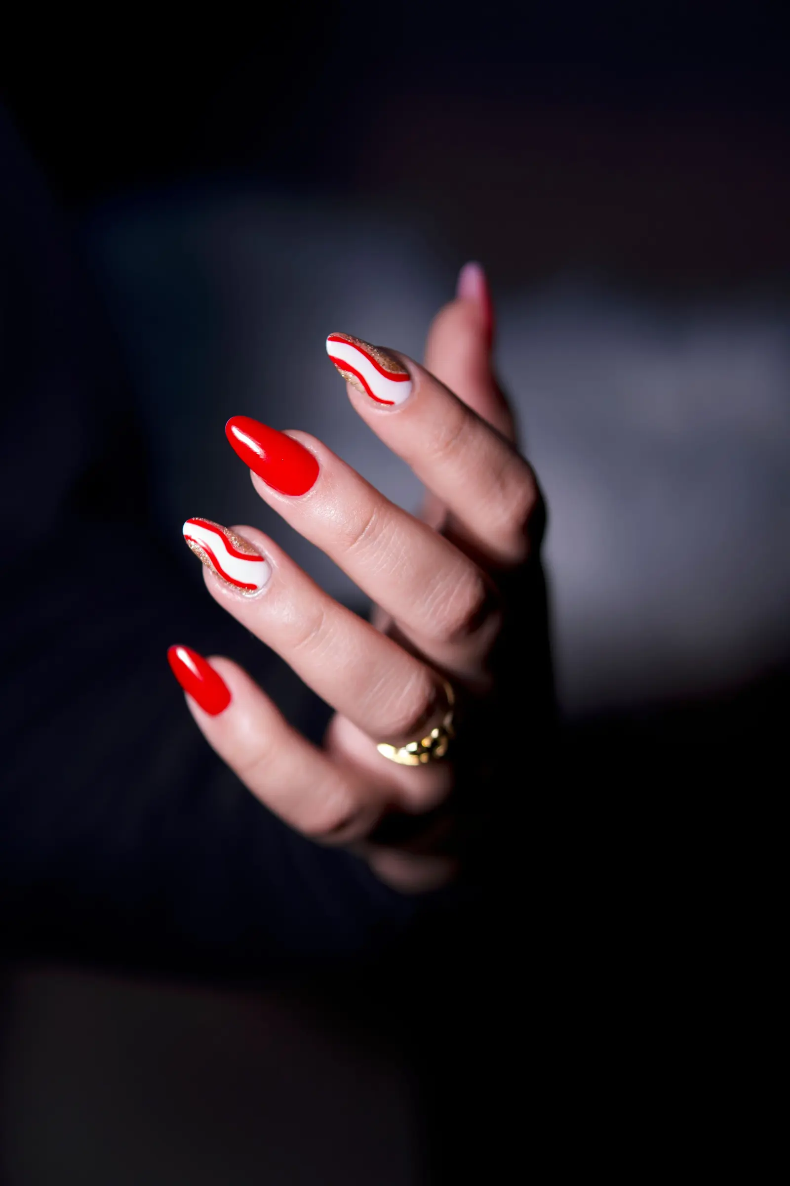 Unghie lunghe rosse e bianche con un disegno a onde, su fondo scuro