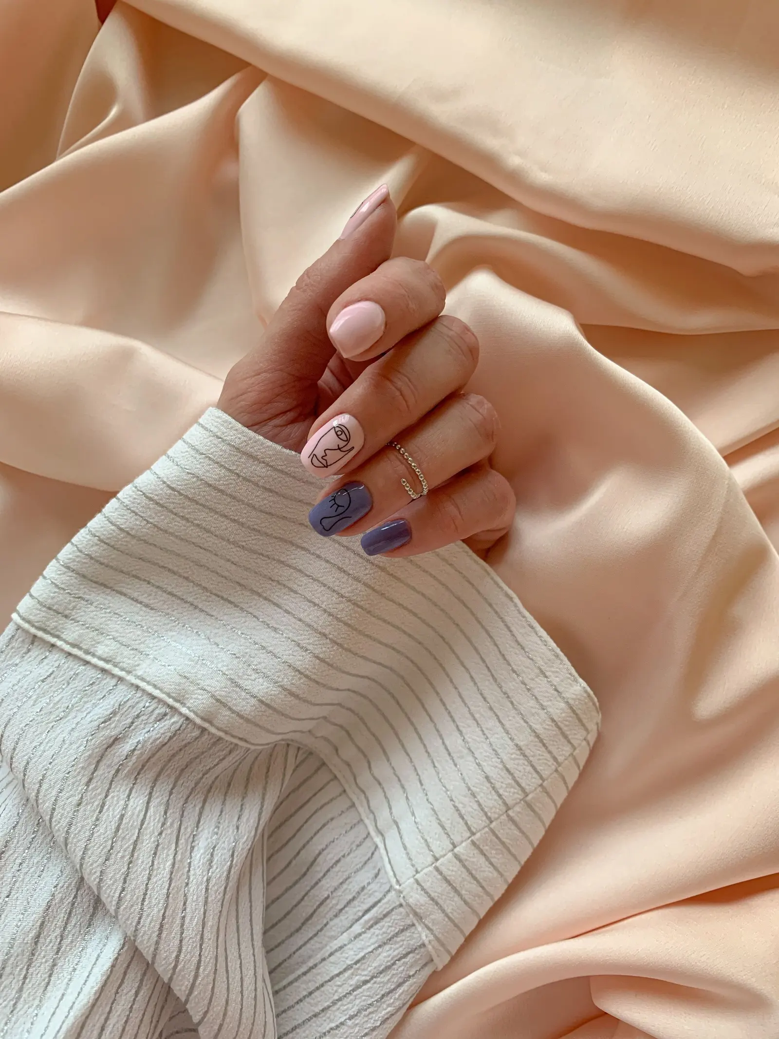 Mano con unghie lilla decorate, su raso color pesca e camicia a righe