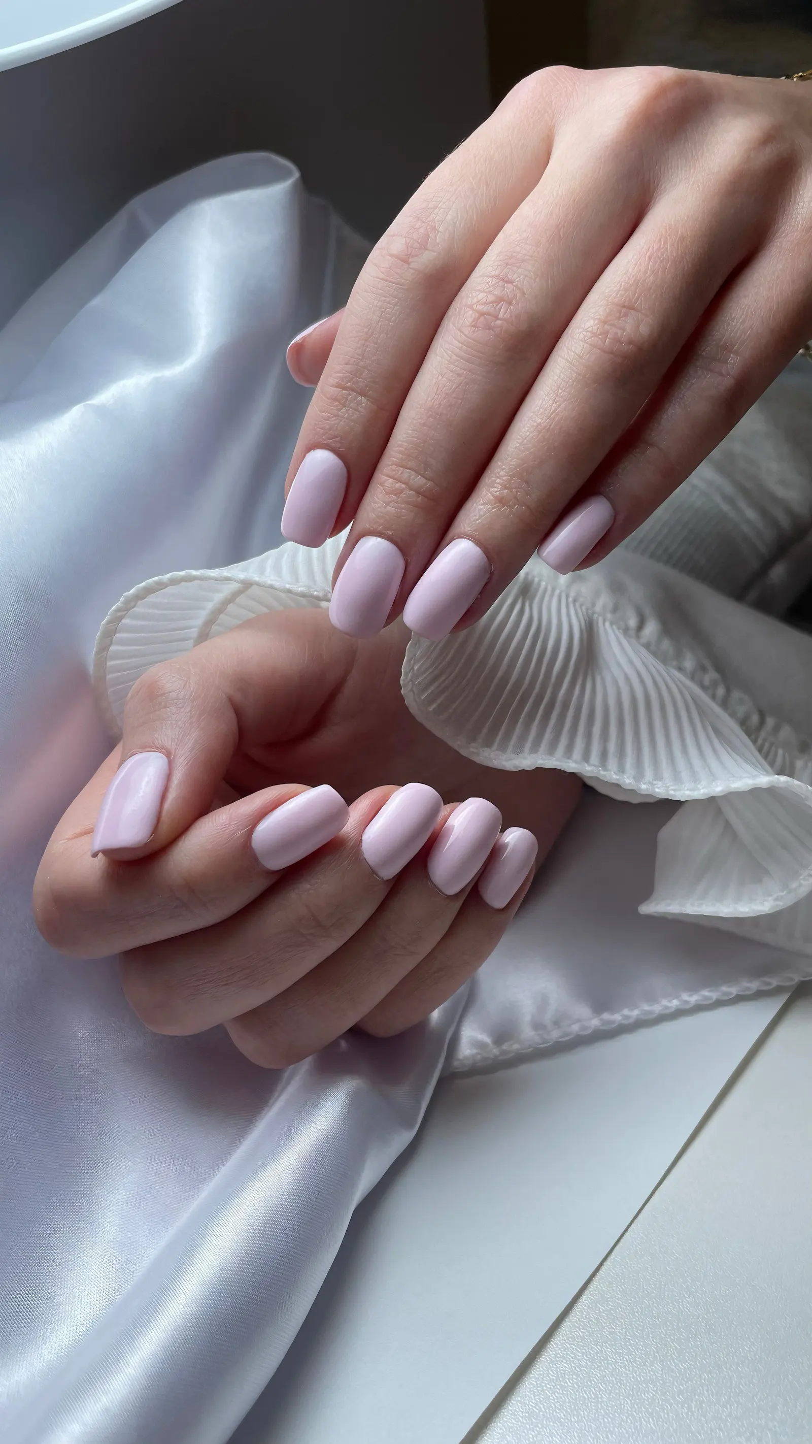 Due mani con smalto rosa chiaro appoggiate su seta bianca