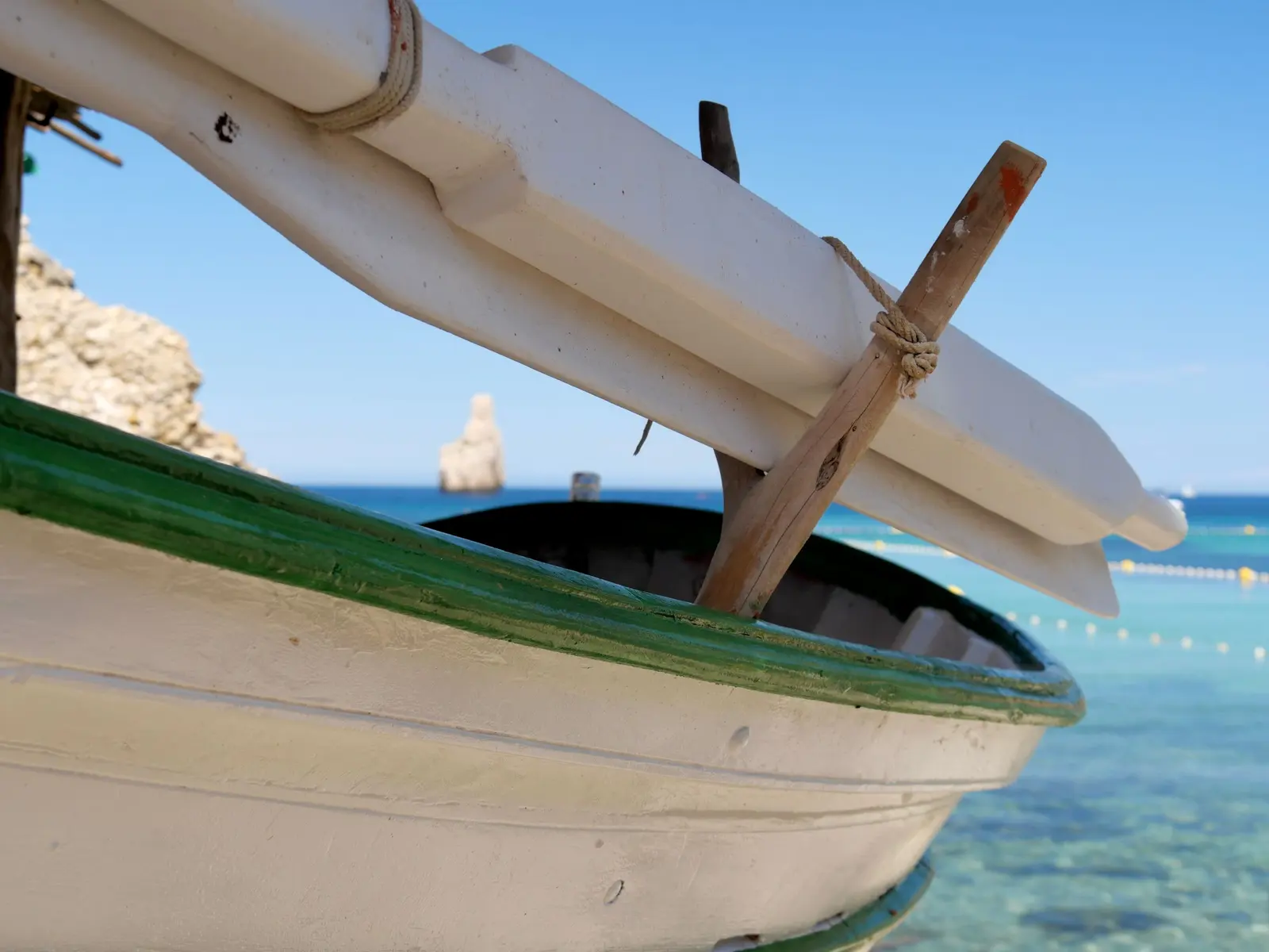 Fianco di una barca da pesca tradizionale bianca con il filetto verde e i remi legati, sopra un mare turchese