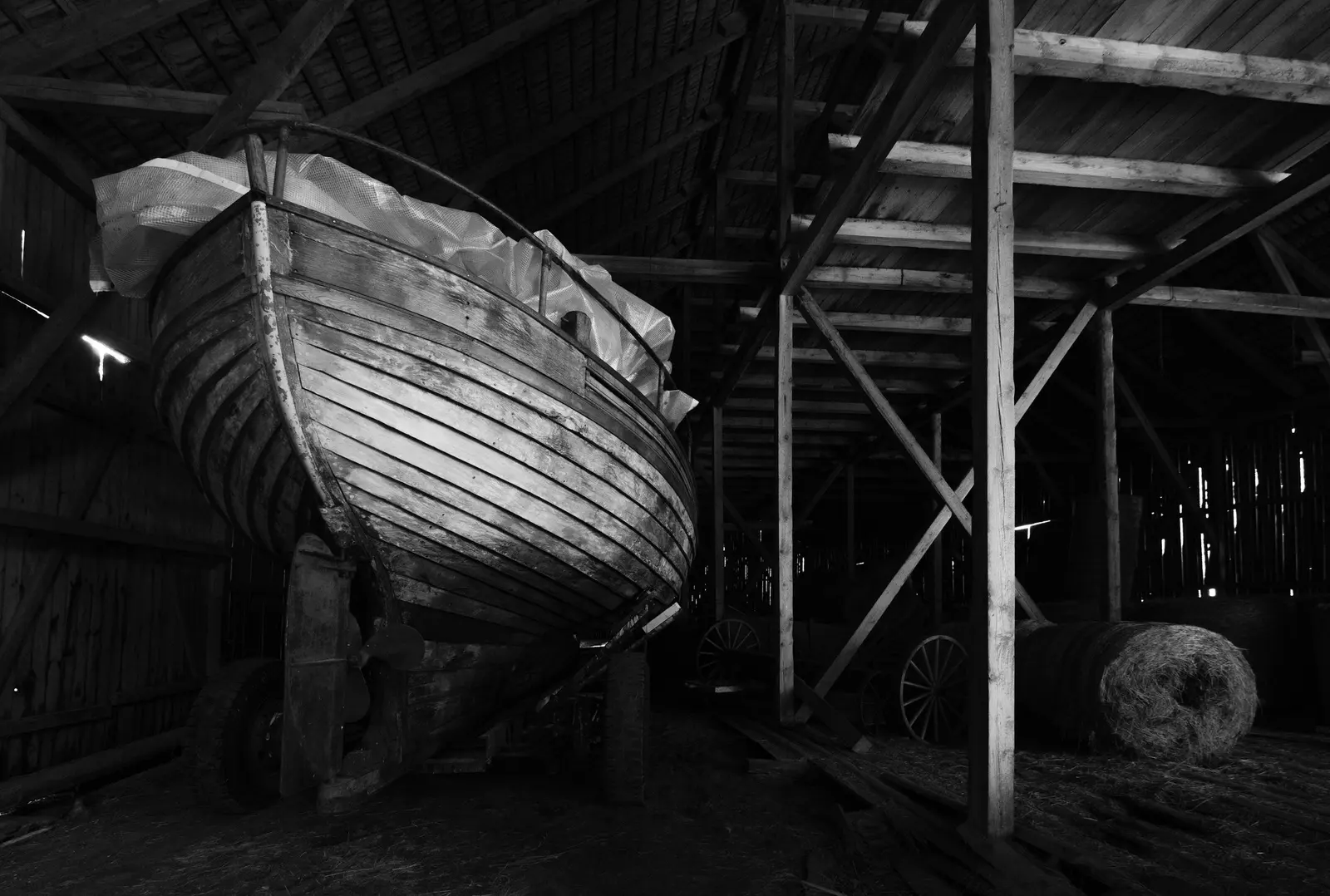 Una barca in legno appoggiata sull'invaso dentro una rimessa di legno, in bianco e nero