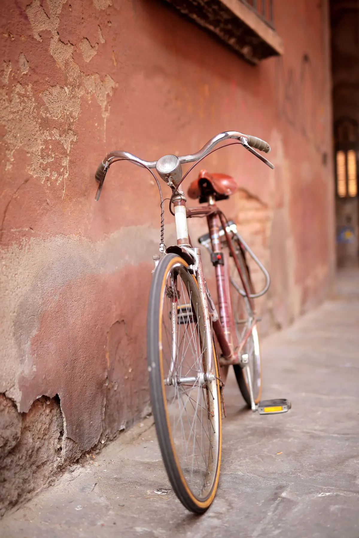 Una vecchia bicicletta appoggiata a un muro color terracotta, in un vicolo