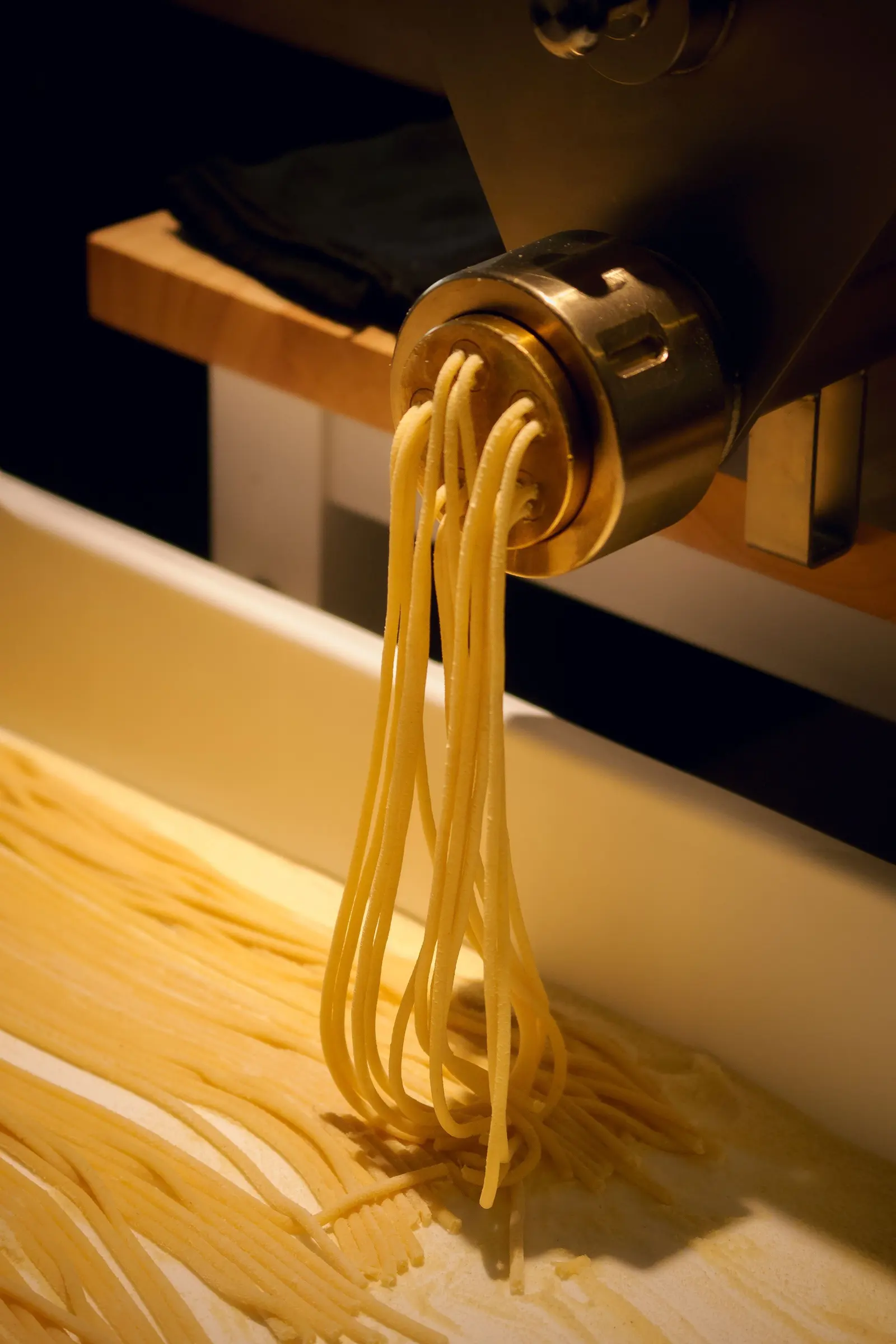 Pasta lunga che esce dalla trafila d'ottone su un piano di legno