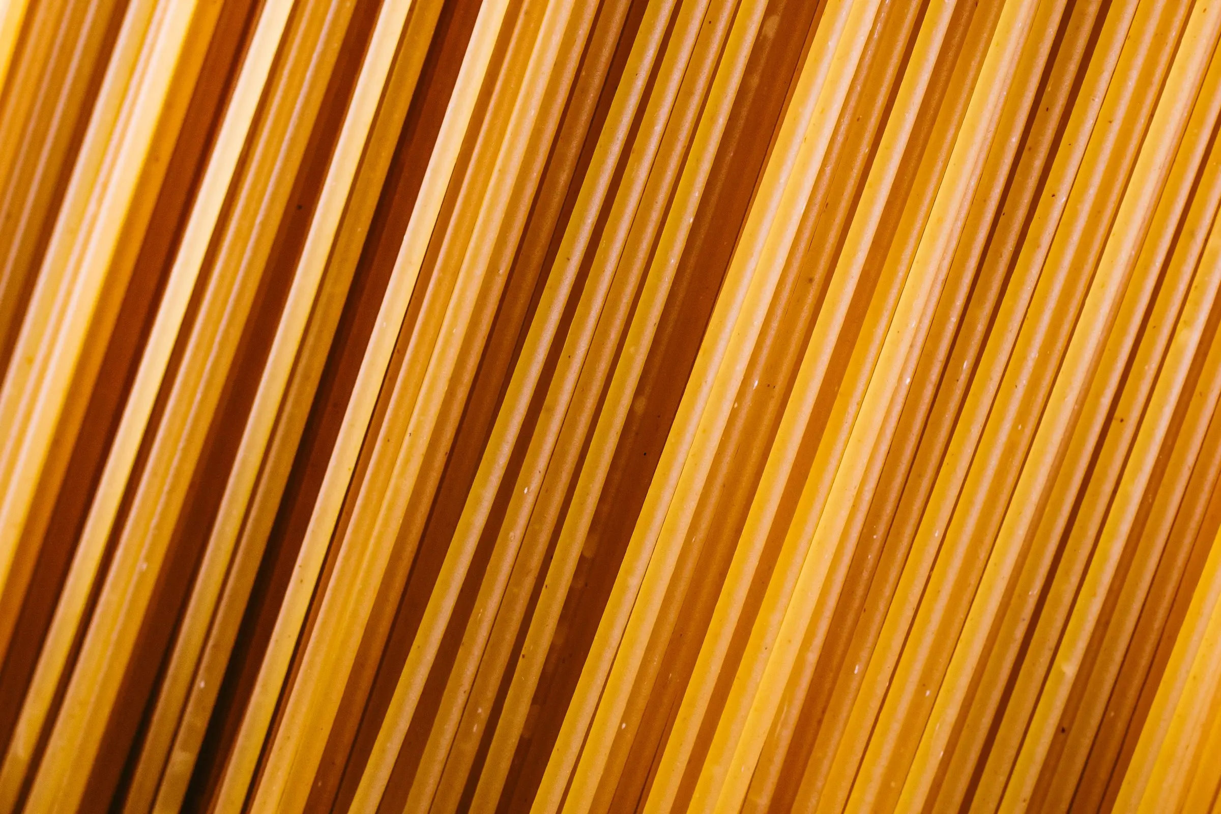 Spaghetti secchi color grano disposti in diagonale, la superficie opaca e ruvida della trafila al bronzo