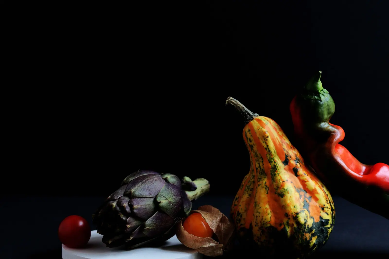 Un carciofo, una zucca ornamentale e un peperone su fondo nero