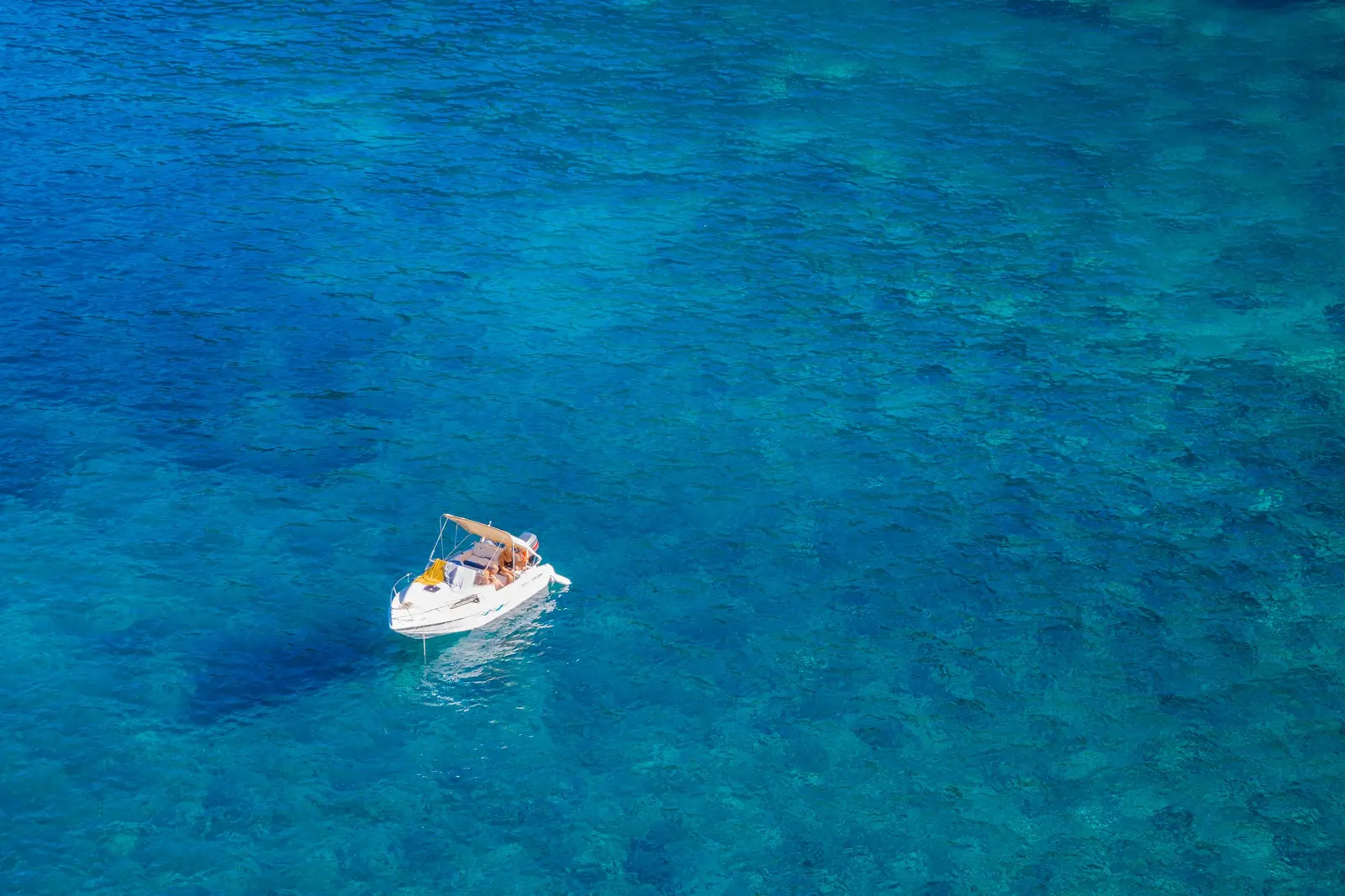 Una piccola barca alla fonda vista dall’alto, sull’acqua limpida e blu