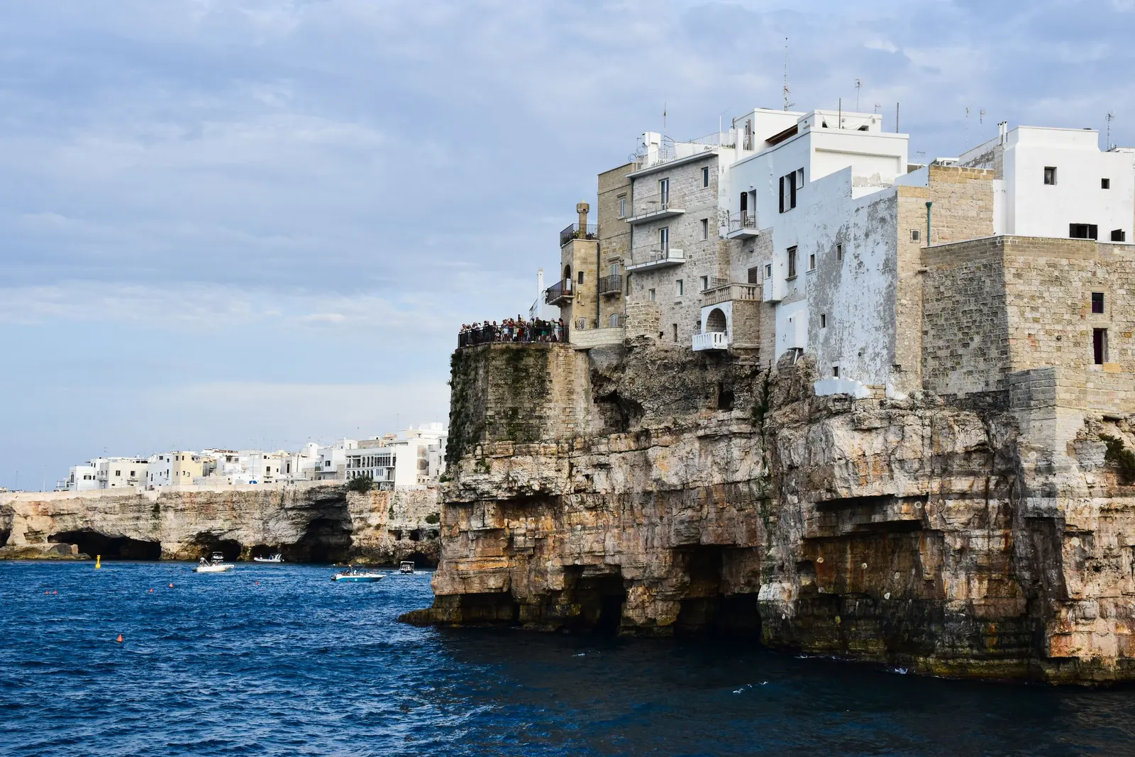 Polignano a Mare dal mare: le case bianche sul bordo della falesia e le grotte che si aprono alla base