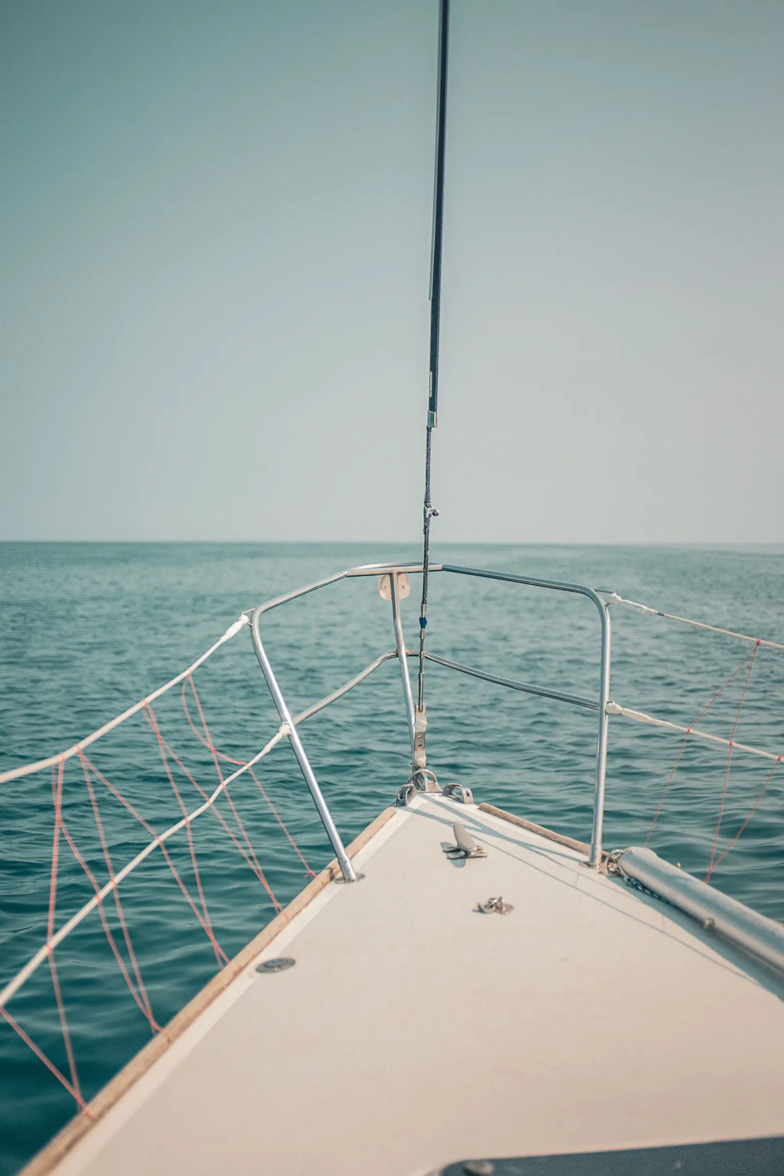 La prua di una barca a vela puntata verso il mare aperto, con l’orizzonte velato