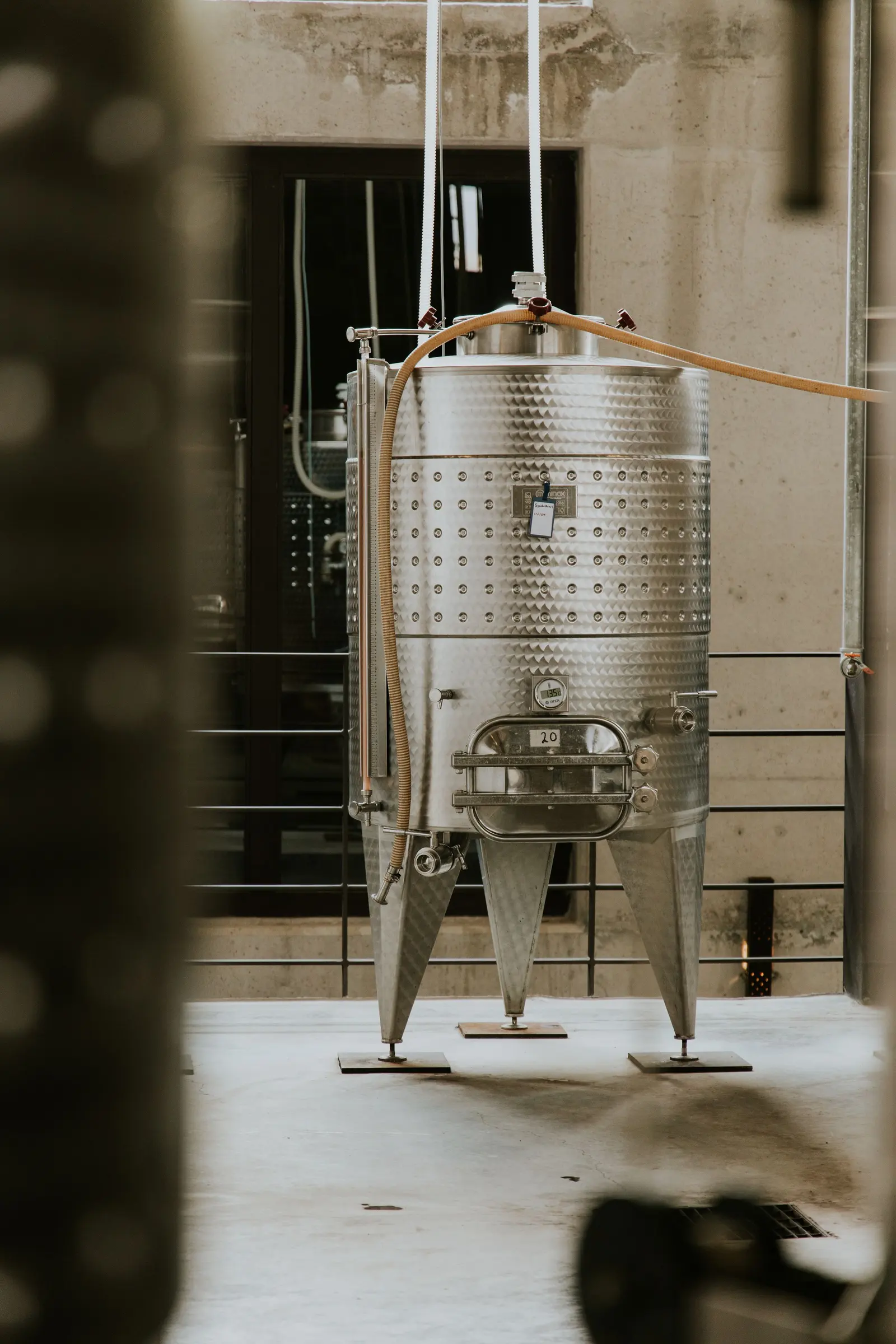 Vasca di fermentazione in acciaio inox con la camicia di raffreddamento, appoggiata sui suoi piedi in cantina