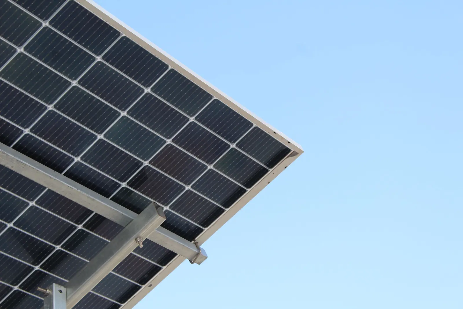 Angolo di una pensilina fotovoltaica vista dal basso: moduli bifacciali e travi zincate contro il cielo