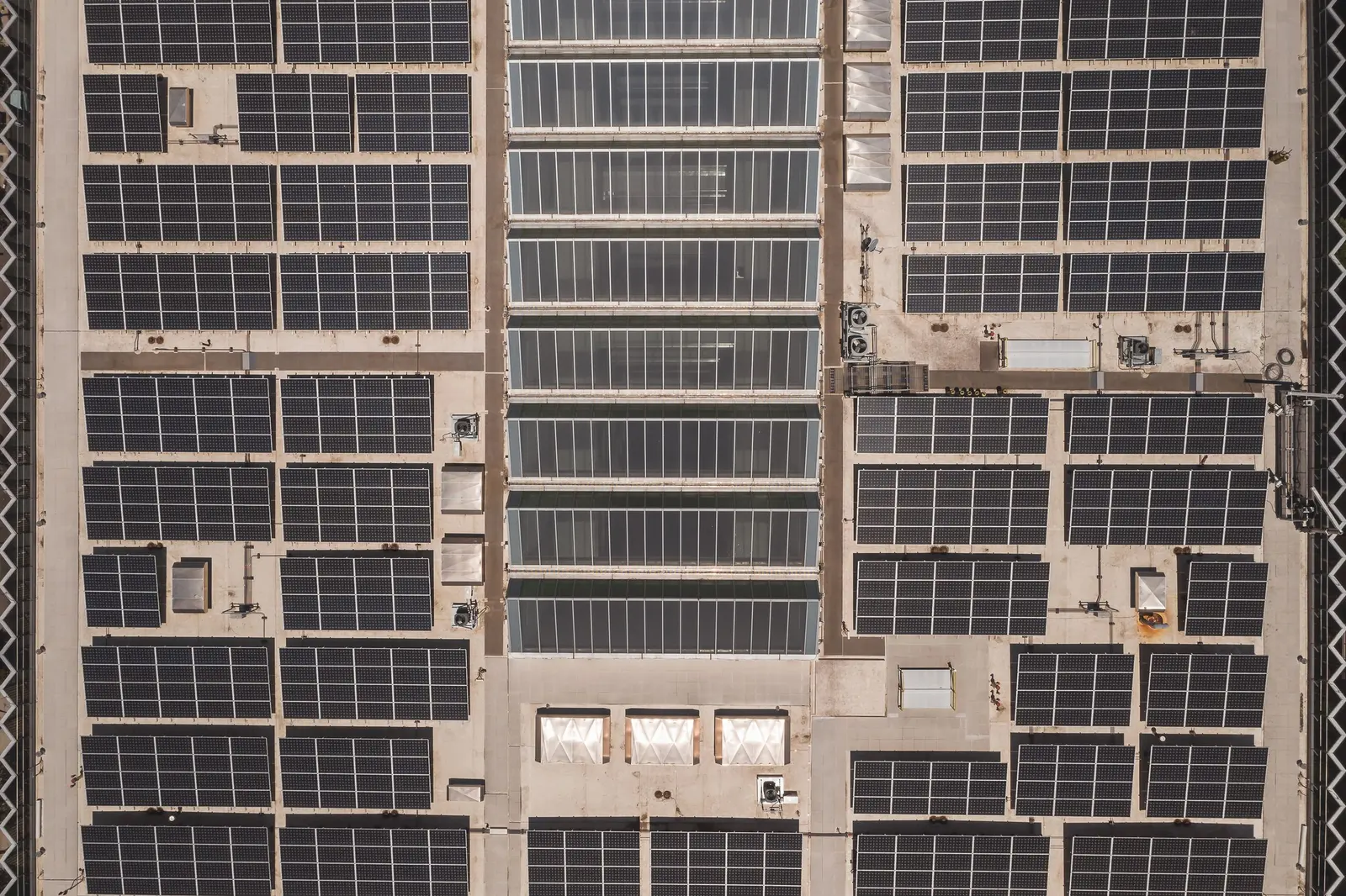 Tetto piano di un edificio commerciale visto dall'alto: file di moduli fotovoltaici tra lucernari e macchine