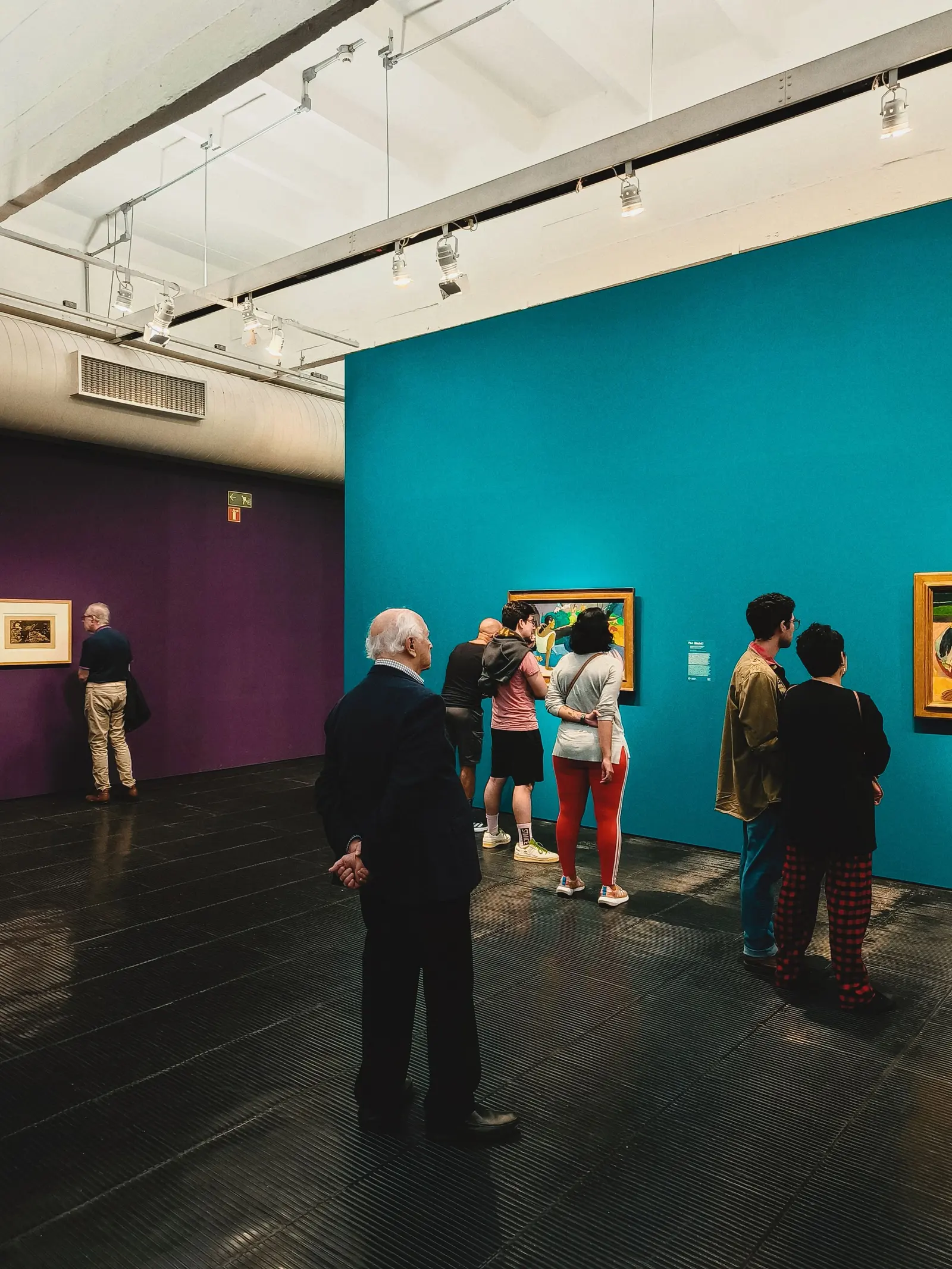 Visitatori in una galleria con pareti turchesi e quadri appesi