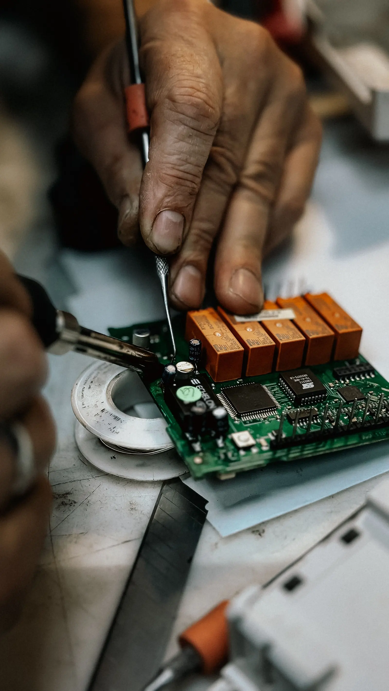 Mani di un tecnico che lavorano su una scheda elettronica con relè, sul banco