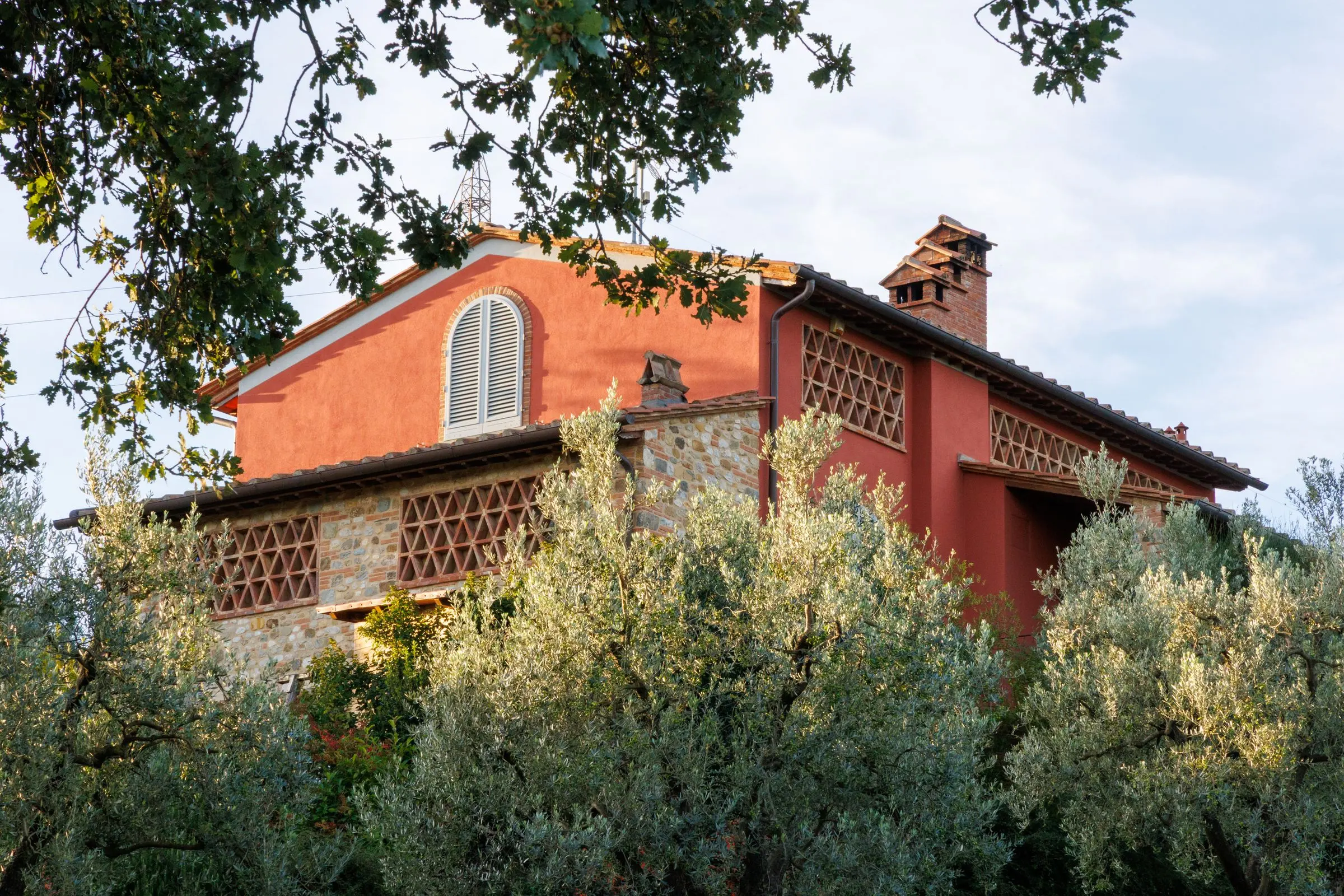 Casale intonacato di rosso con grigliati in mattone, tra gli ulivi