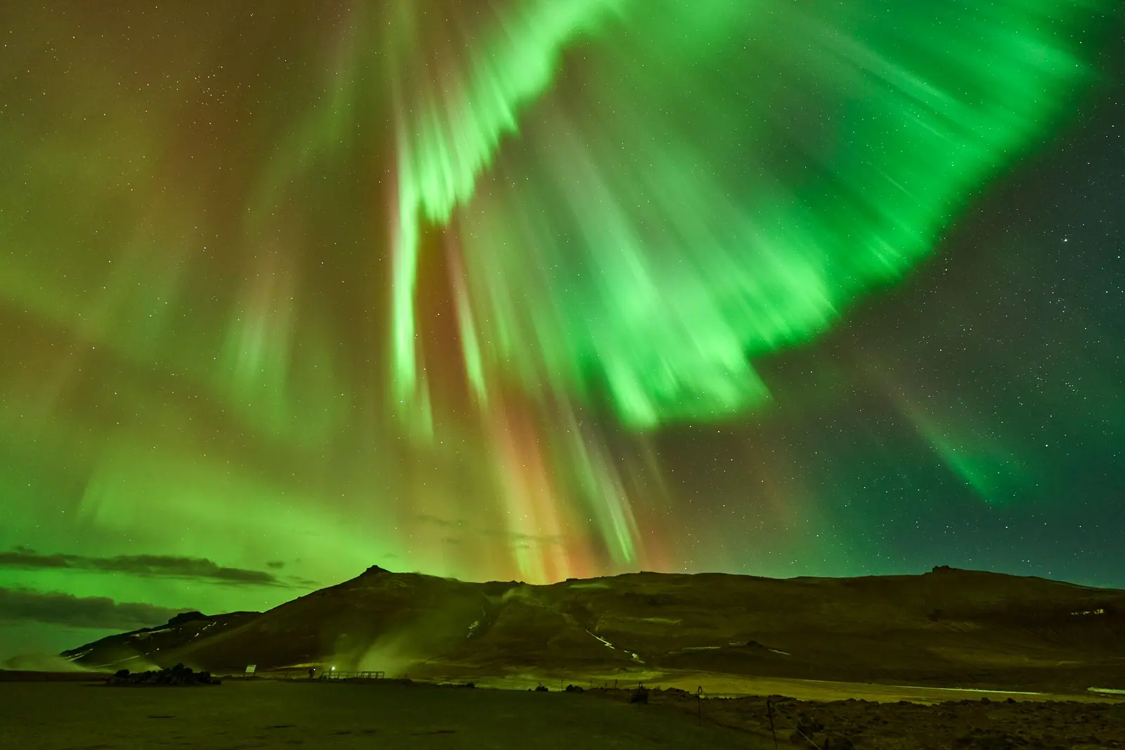 Un'aurora boreale verde che riempie il cielo notturno sopra colline coperte di neve