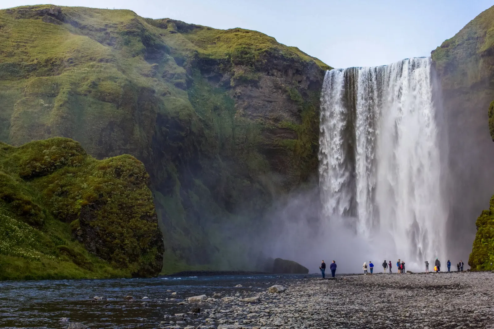 Una grande cascata che precipita tra due pareti verdi, con un gruppo di persone piccolissime alla base