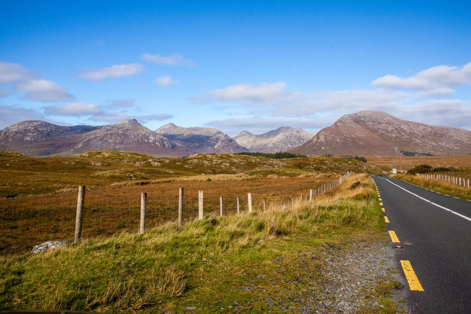 Una strada di campagna con la riga gialla nel Connemara, con montagne brulle e cielo azzurro