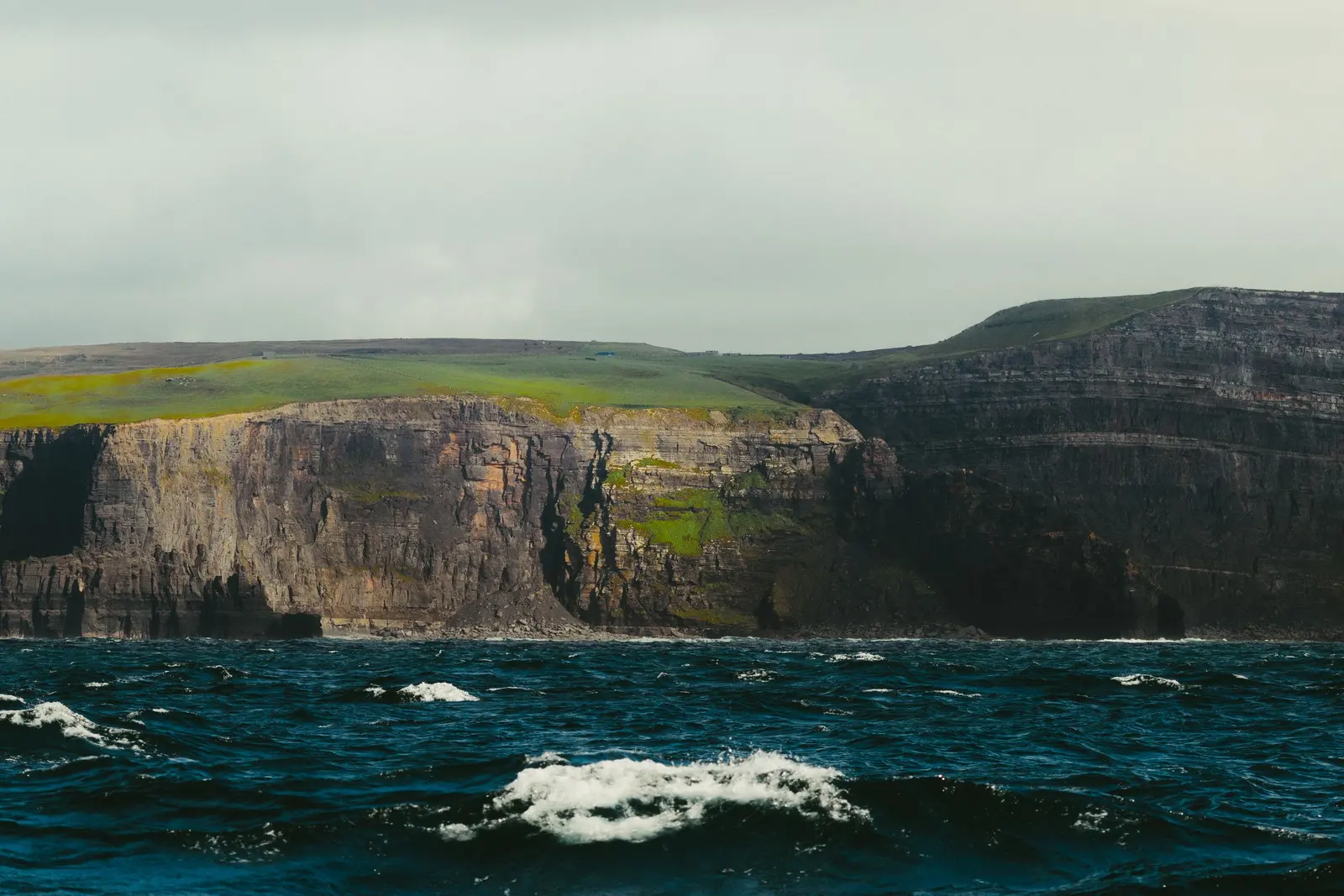Scogliere verticali a picco sull'oceano mosso nelle isole Aran, il prato verde in cima
