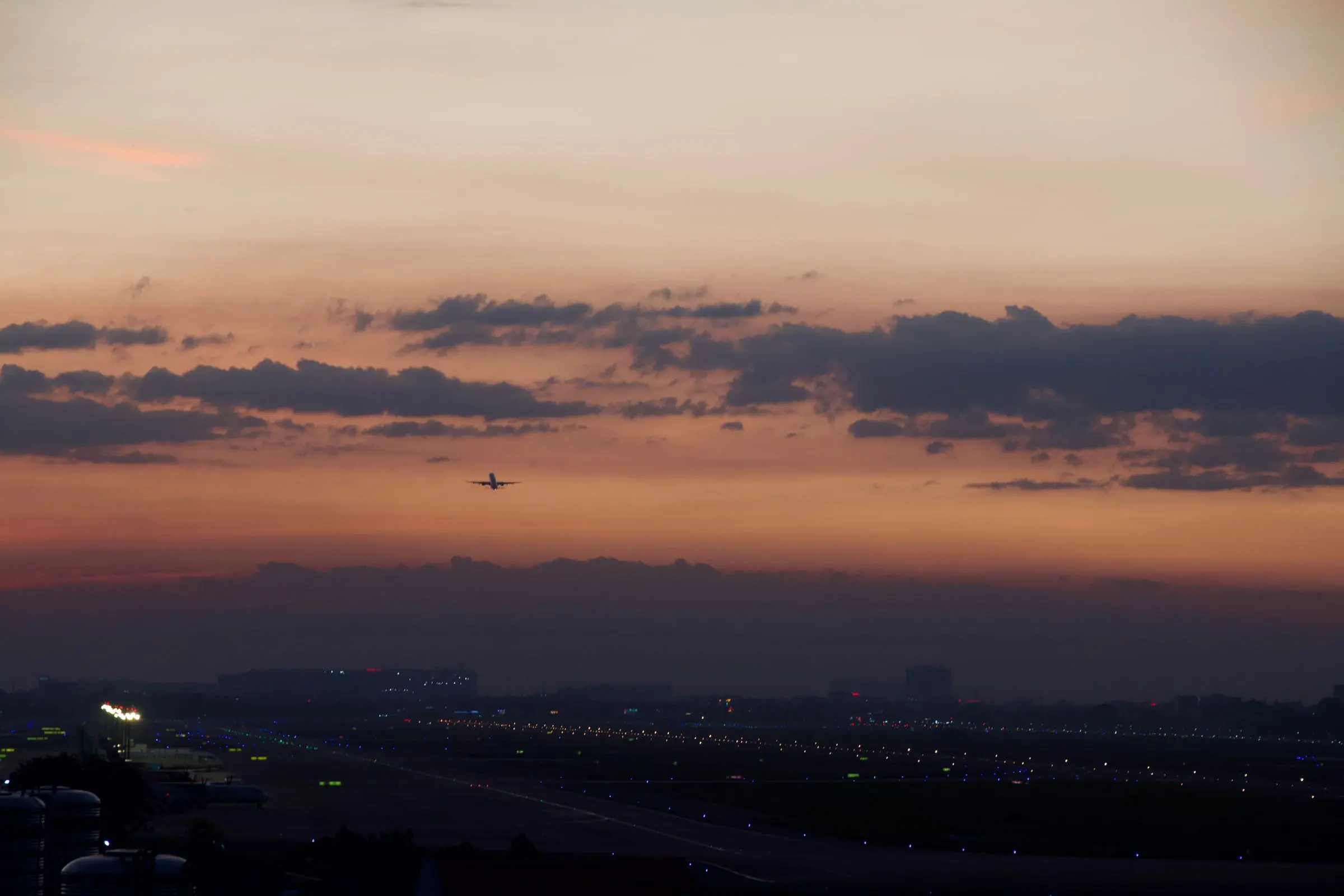Il cielo dell'alba, rosa e sabbia, sopra un aeroporto: un aereo piccolo in avvicinamento e le luci della pista