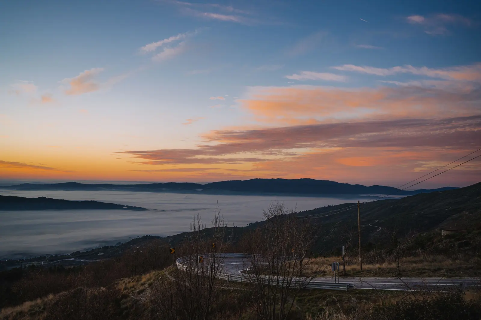 Una strada di collina all'alba, con la nebbia nelle valli e il cielo rosa