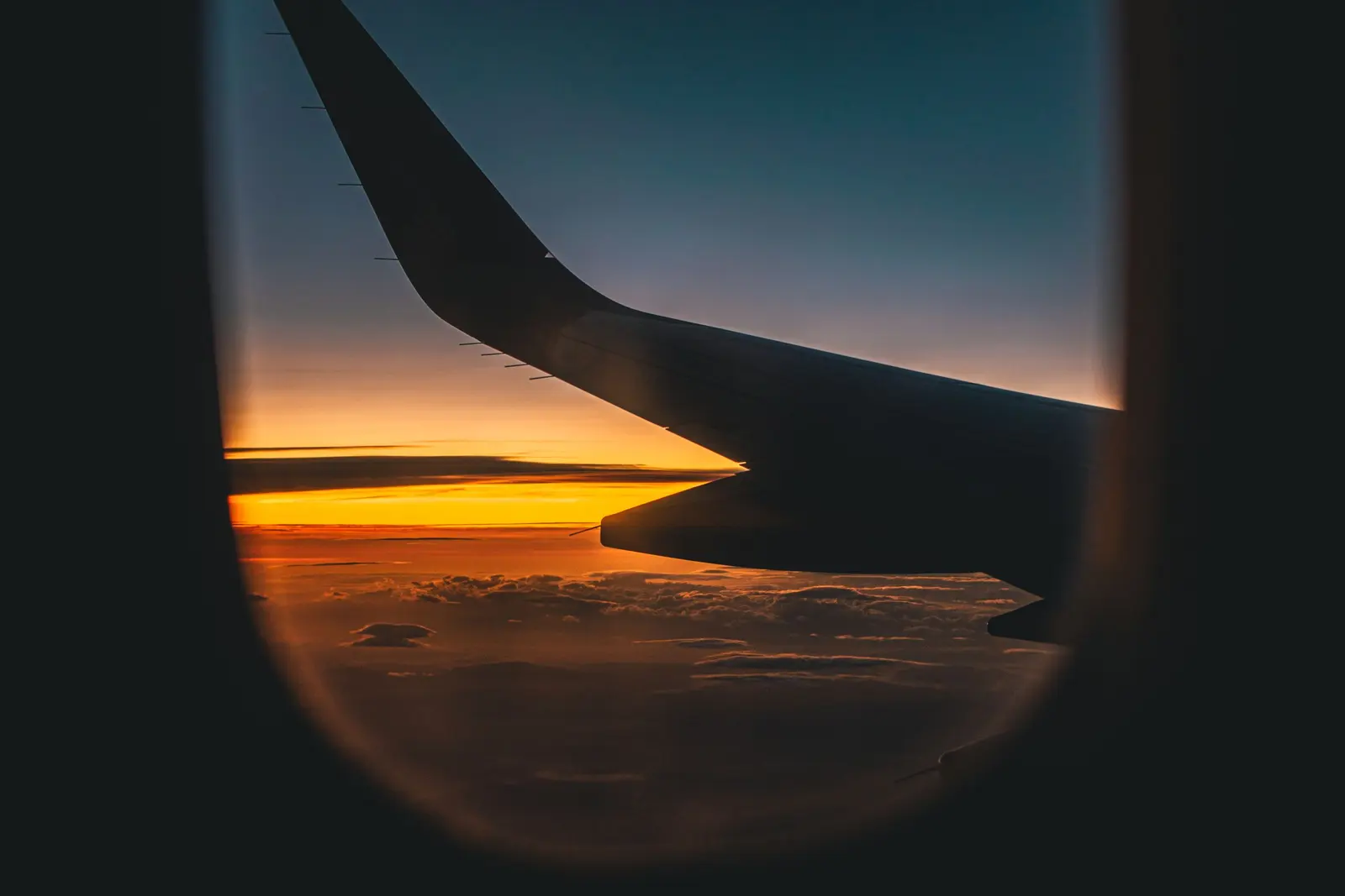 Dal finestrino di un aereo, l'ala in controluce e il tramonto sopra le nuvole