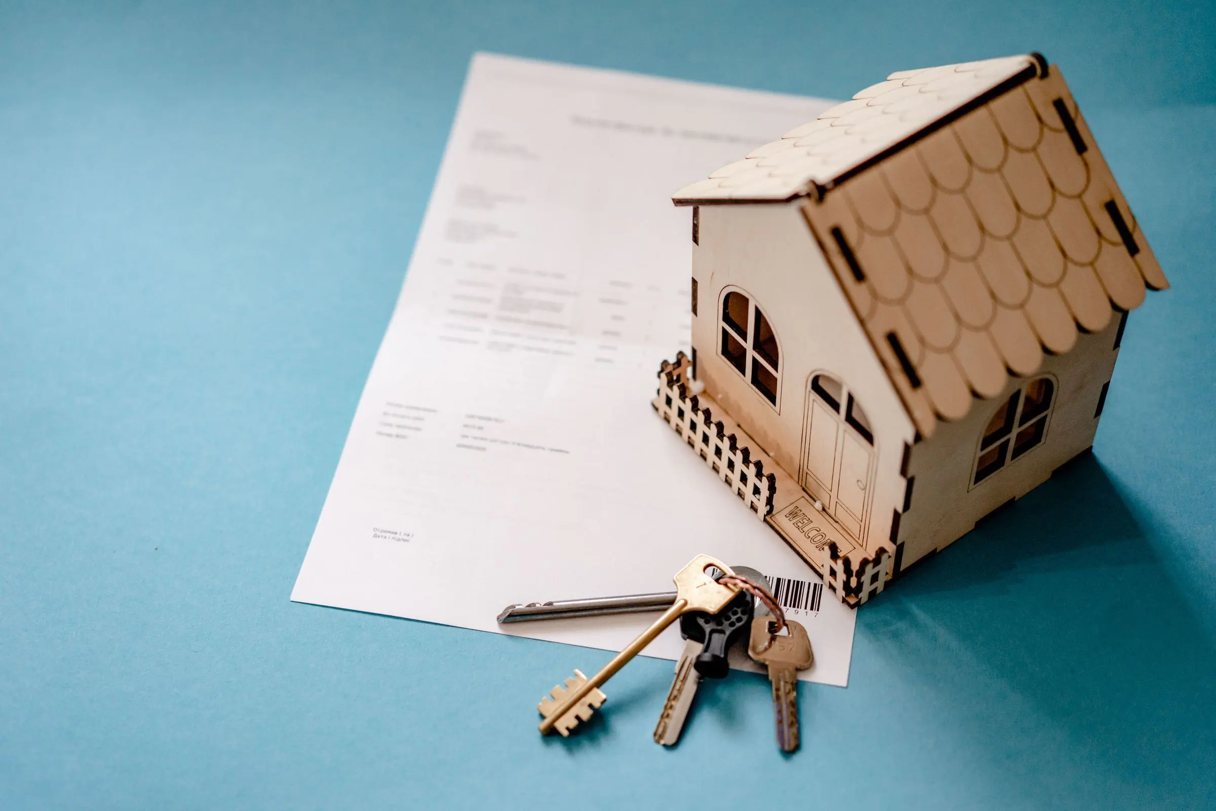 Modellino di una casa in legno con un mazzo di chiavi appoggiato su un contratto