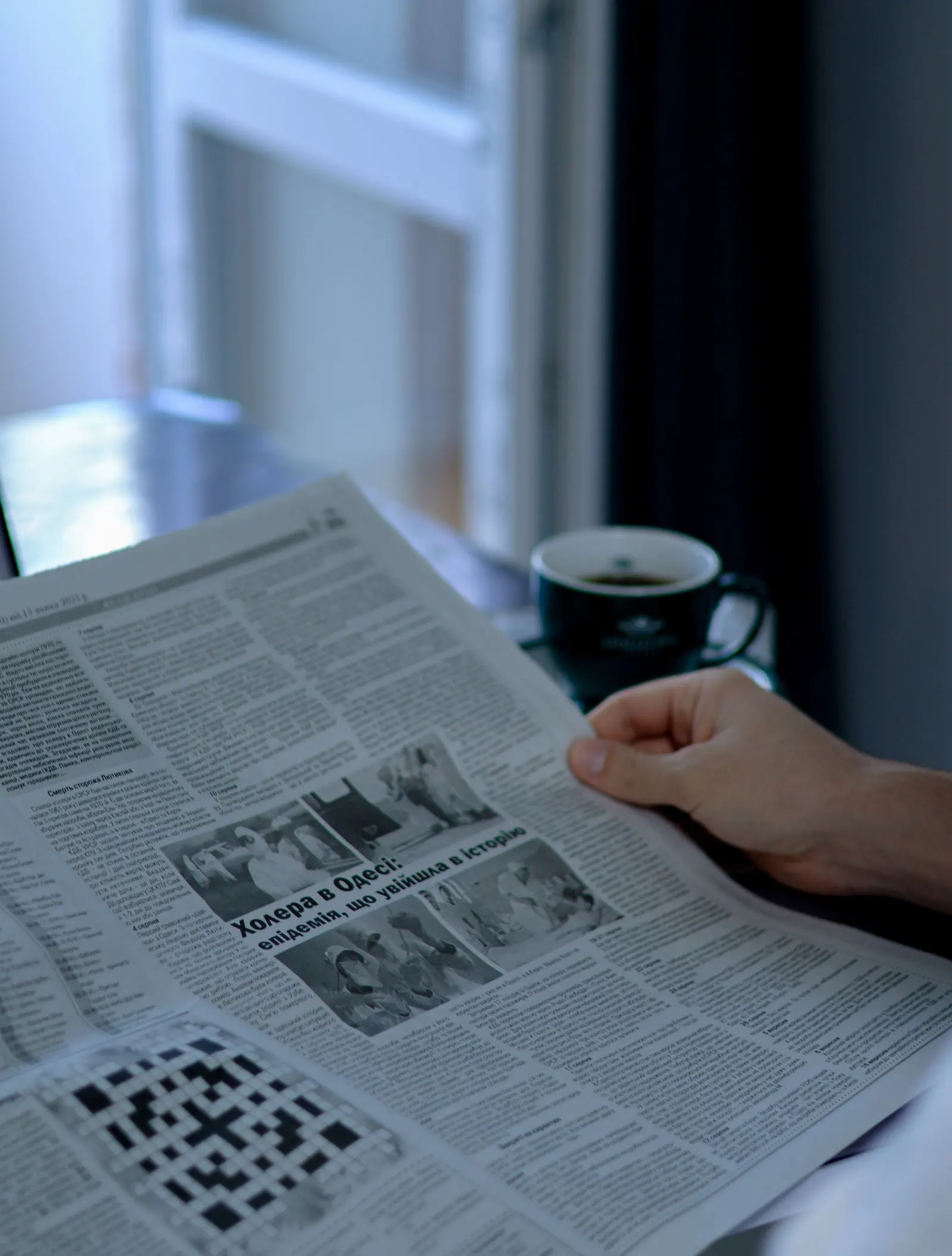 Una mano tiene un giornale aperto vicino alla finestra