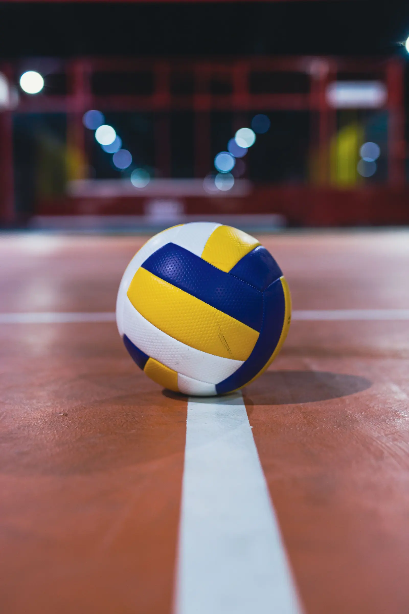 Un pallone da pallavolo fermo sulla linea del campo, con le luci del palazzetto sfocate