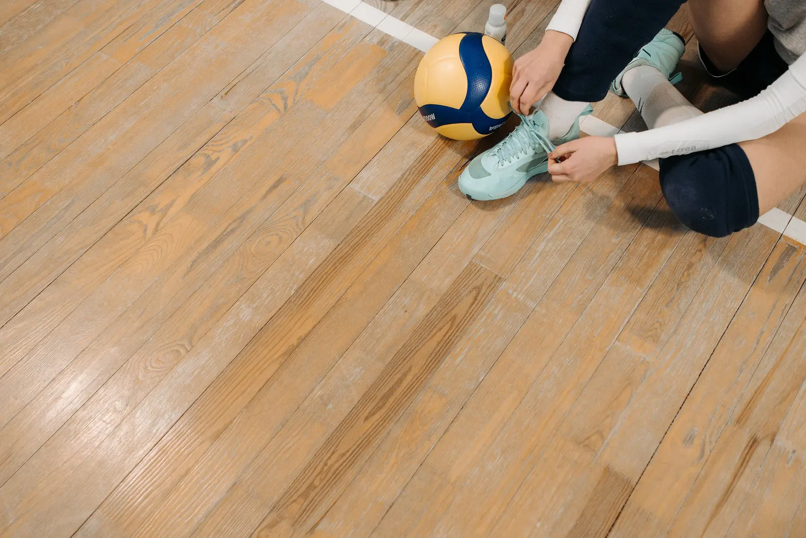 Scarpe da pallavolo allacciate sul parquet accanto al pallone