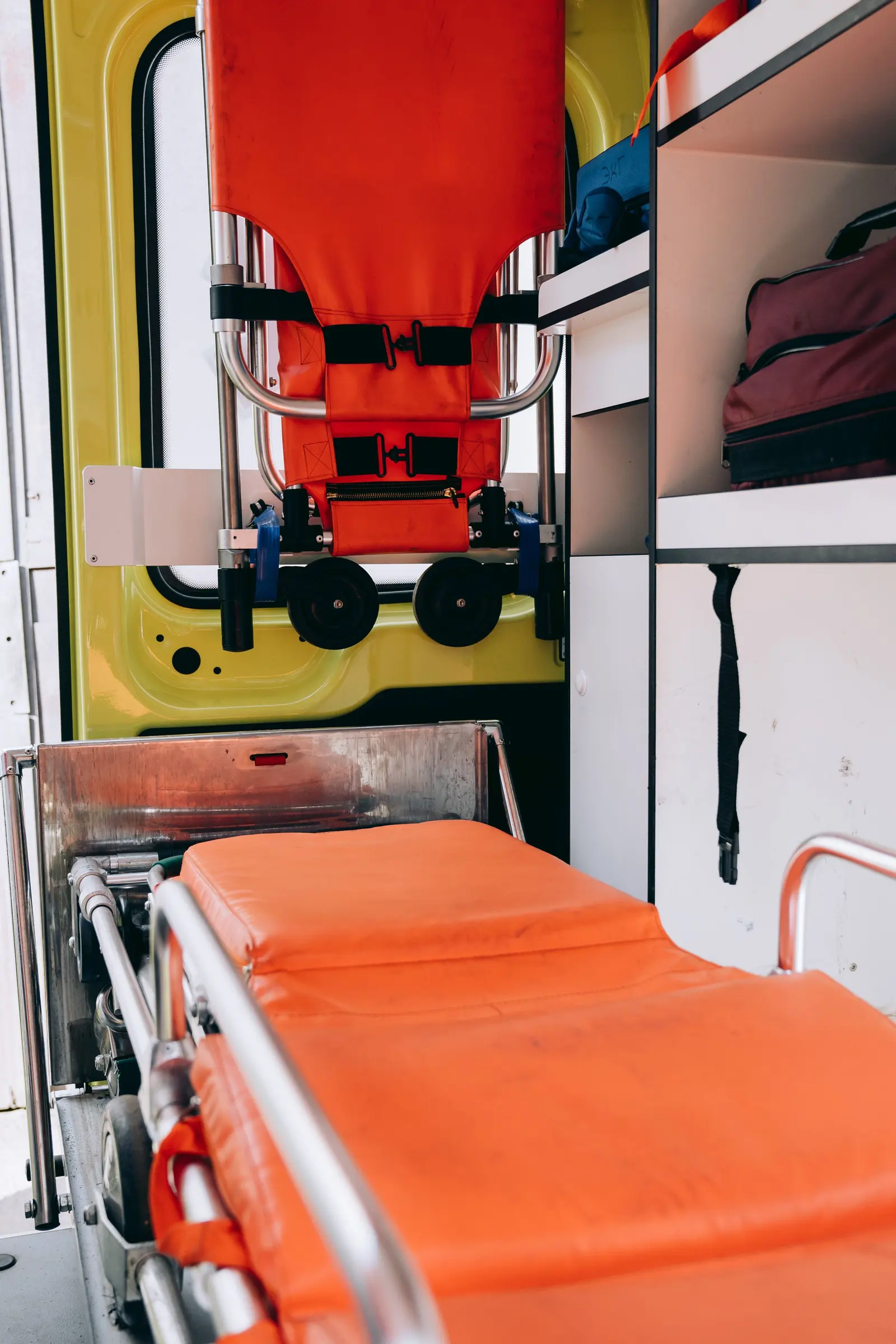 Interno di un vano sanitario: una barella arancione, la sedia portantina fissata al portellone giallo, i pensili bianchi