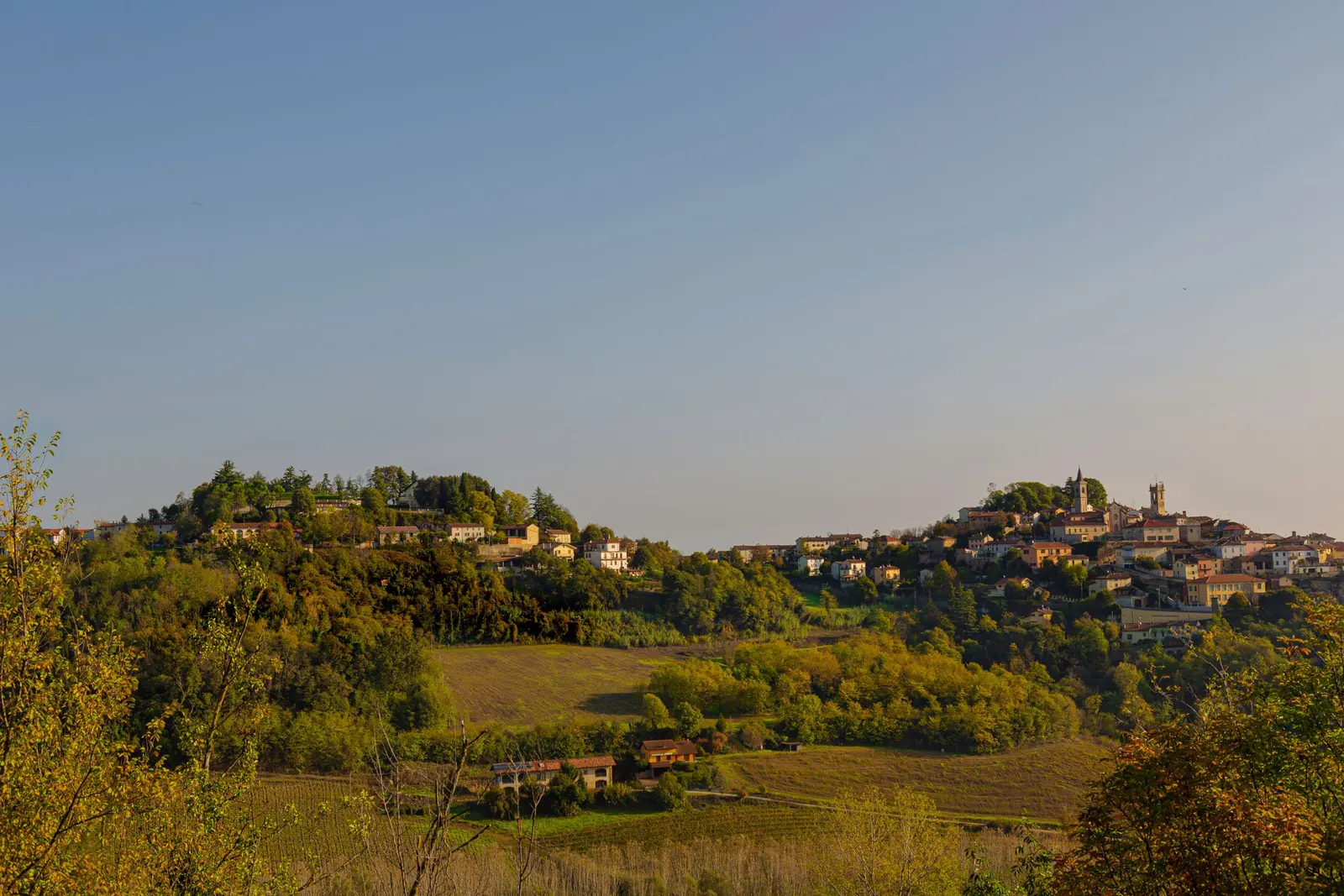 Un paese in cima a una collina tra boschi e campi, nella luce del tardo pomeriggio