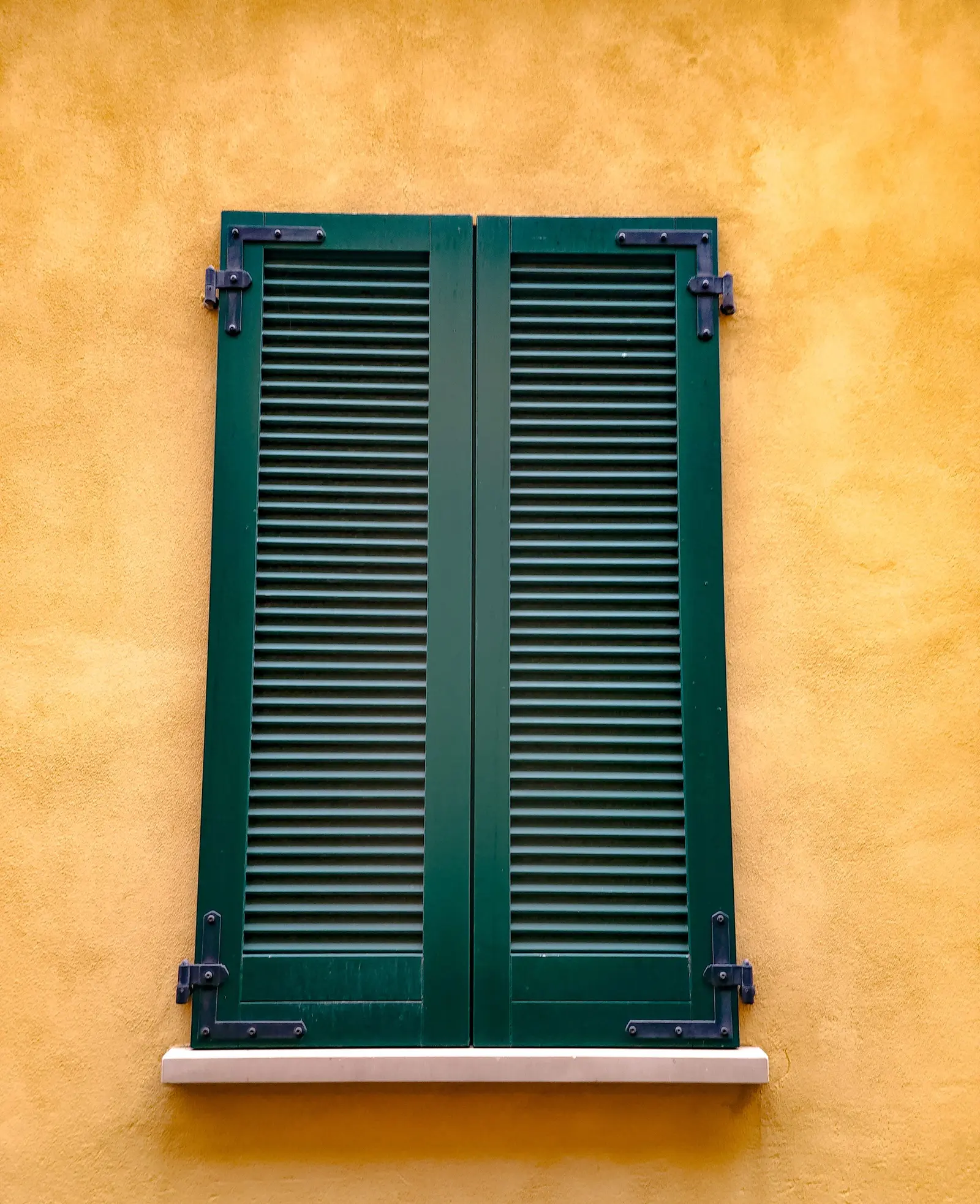 Una persiana verde chiusa sul muro giallo ocra della casa