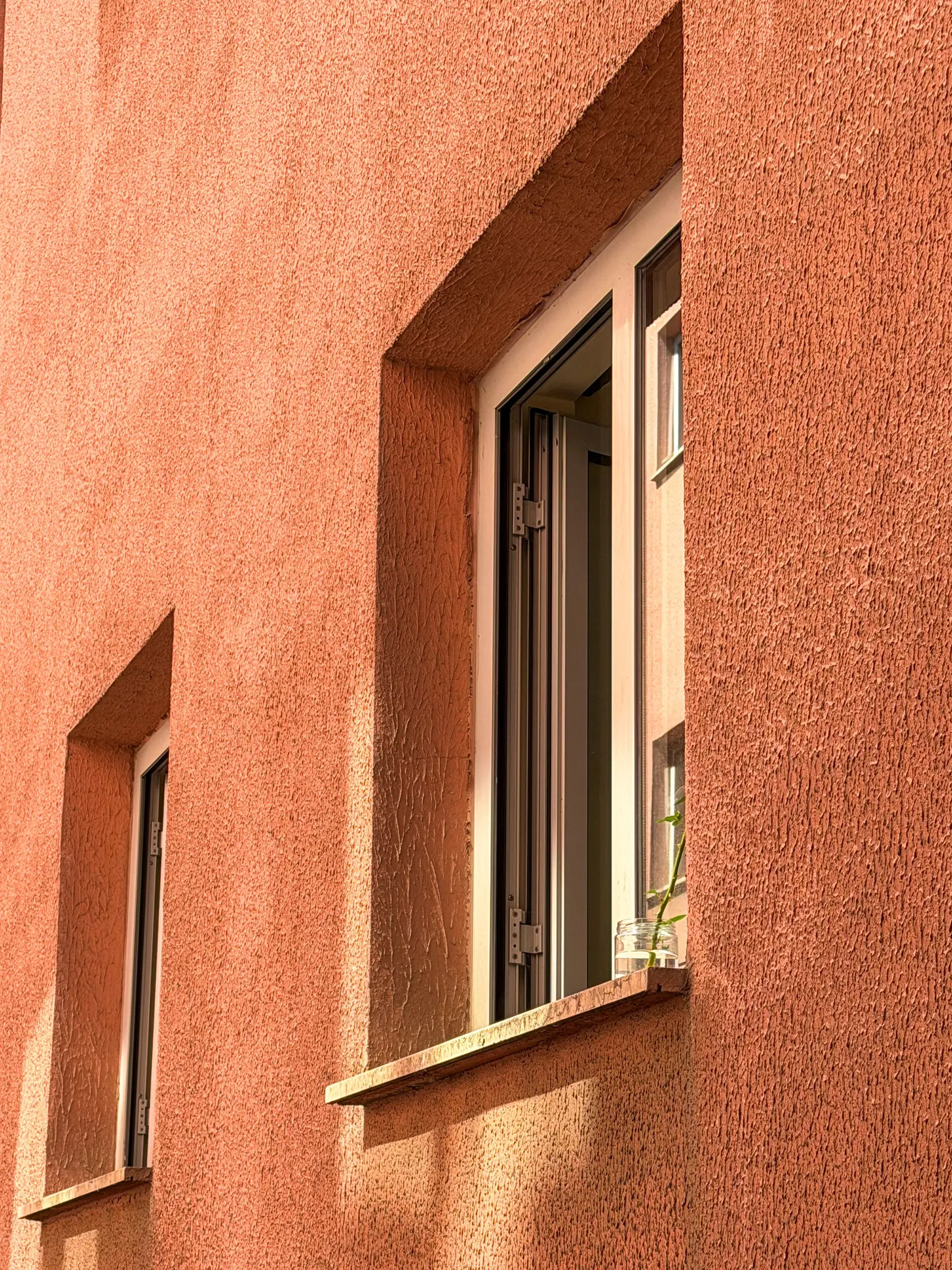 Una facciata con l'intonaco color terracotta e due finestre in legno chiaro, illuminata dal sole radente