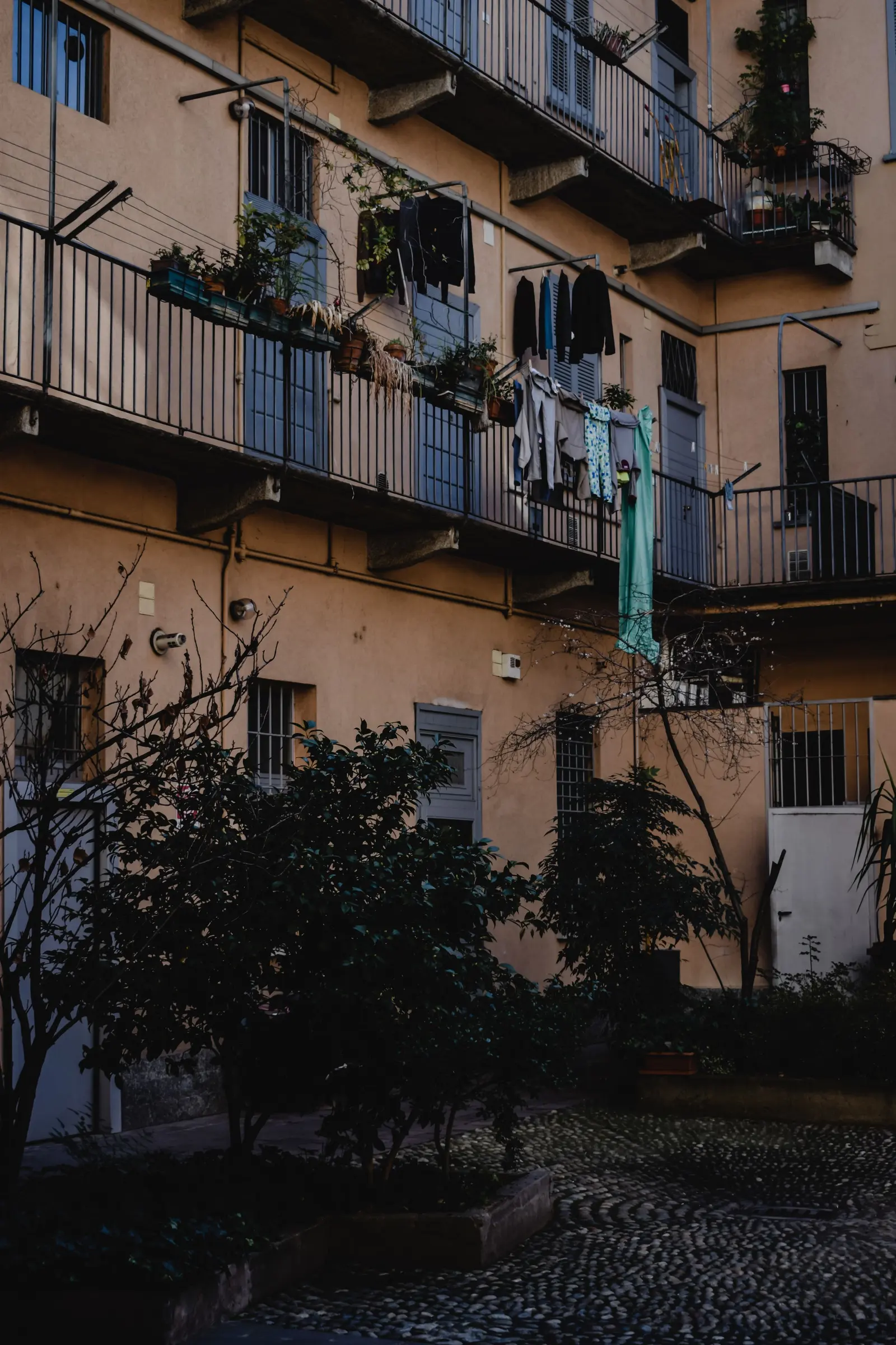 Cortile di una casa di ringhiera milanese, con ballatoi in ferro, piante e panni stesi