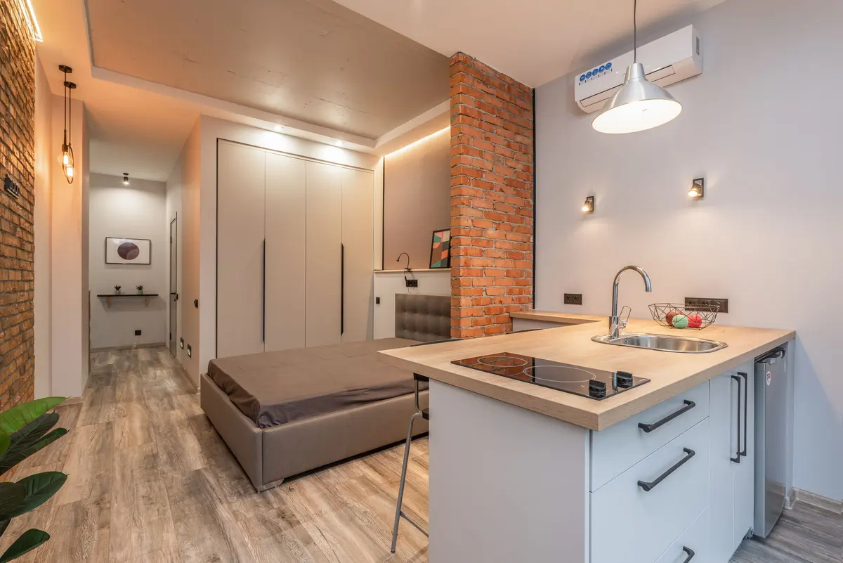 Monolocale con parete in mattoni, isola della cucina e letto sullo sfondo