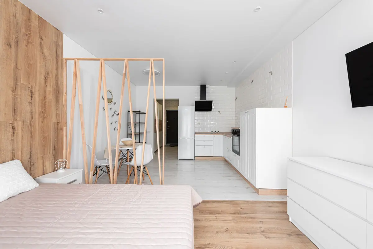 Monolocale bianco con letto matrimoniale, separé in legno e cucina sul fondo