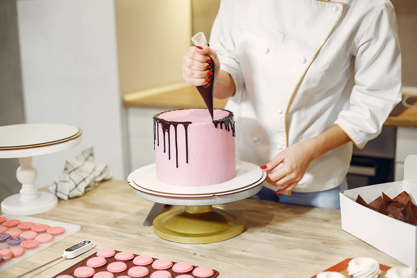 Una pasticcera, di cui si vedono solo mani e grembiule, cola la ganache su una torta rosa