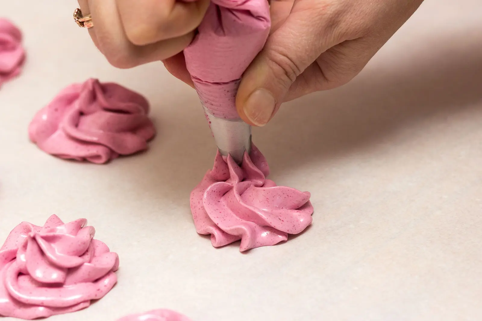Mani che spremono meringhe rosa sulla carta da forno