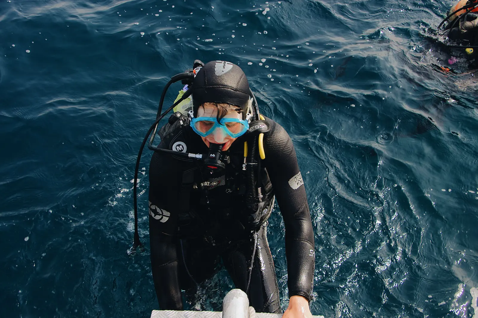 Un sub con la maschera azzurra risale la scaletta di una barca dopo un'immersione in mare aperto